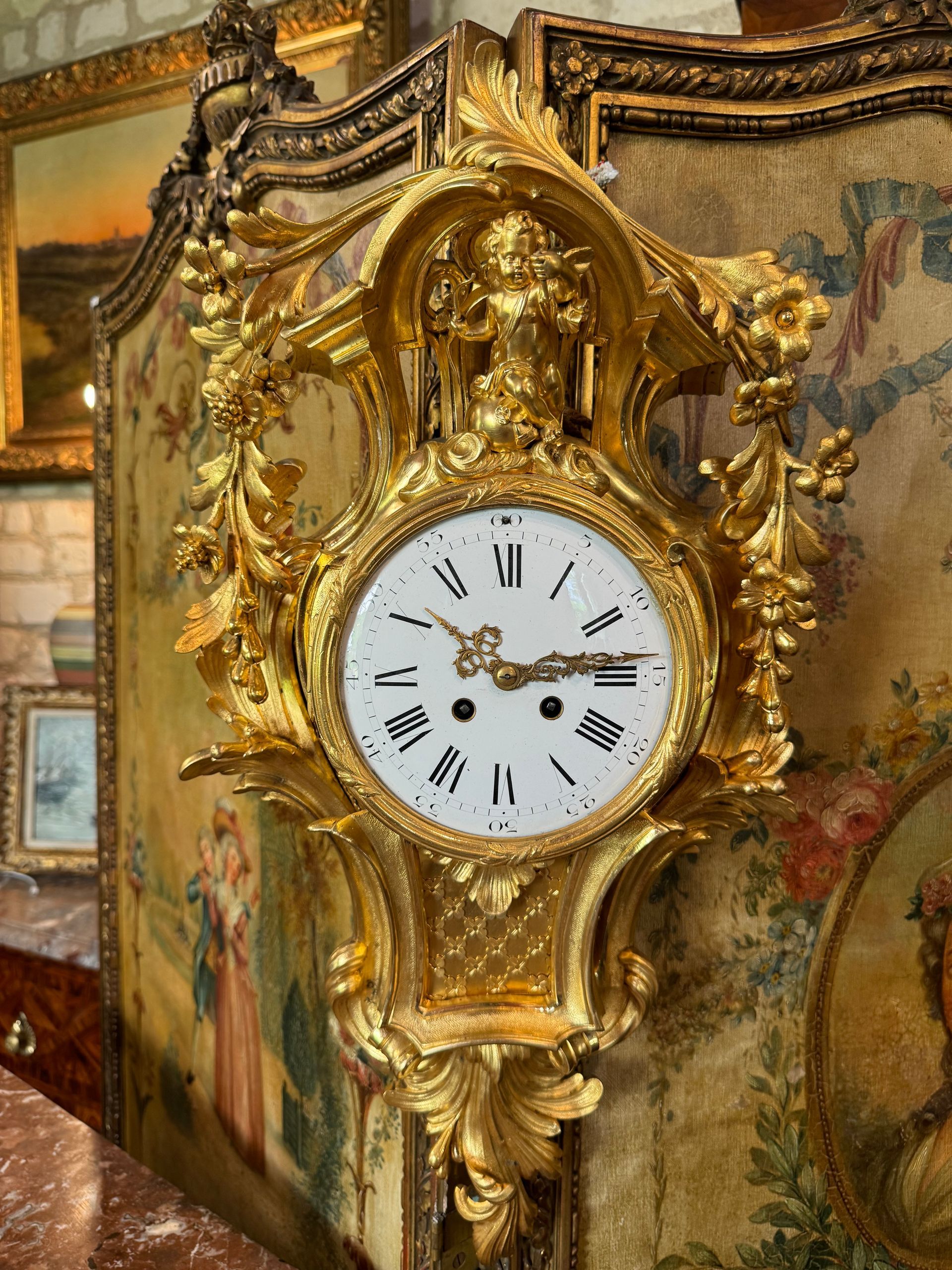 Cartel d'applique fortement mouvementé, en bronze doré, de style Louis XV - 19ème,
A décor de feuillages, enfants et fleurs,
Cadran émaillé à chiffres romains,
Dorure d'origine.