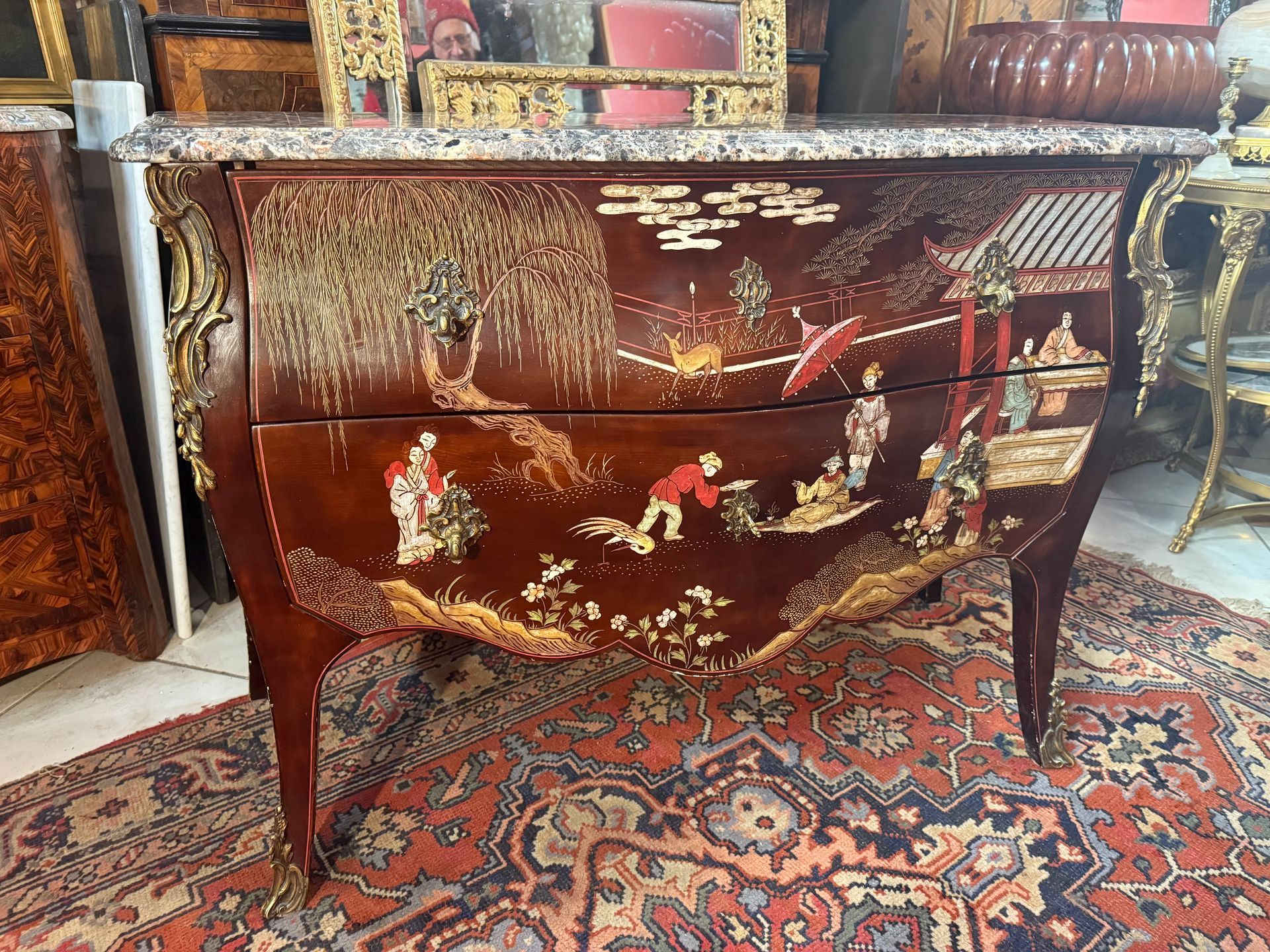 Commode de style louis XV, travail du début 20ème en laque de chine sur fond brun,  à décor principal de différentes scènes de personnages chinois, animaux en facade et sur les cotés.
Poignées et chutes de bronze ciselées et dorées,
Cette commode est galbée en façade et sur les côtés, 
Elle ouvre par deux tiroirs sans traverse
Le tout coiffé d'un marbre brèche
