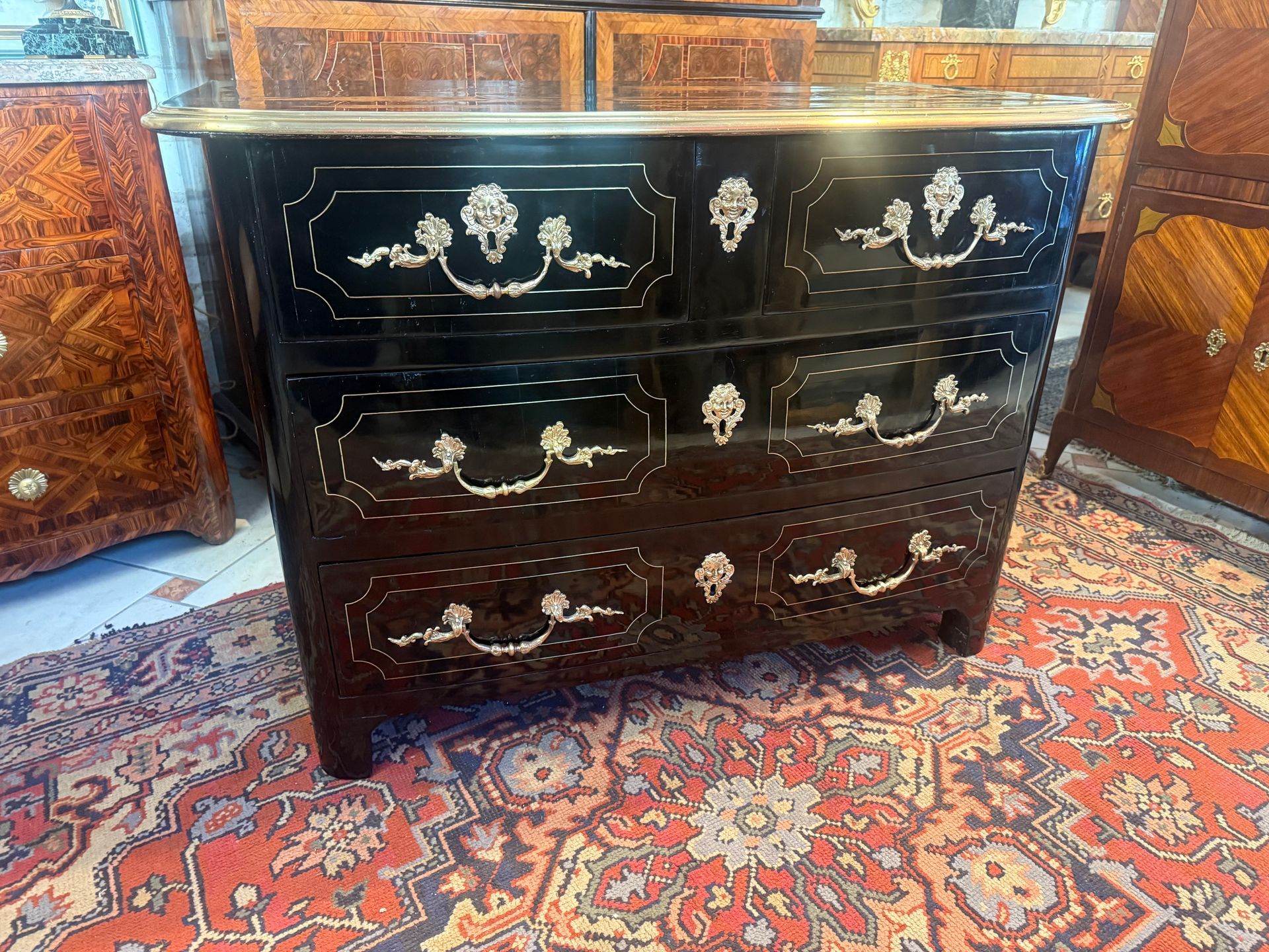 Commode Louis XIV de forme cintrée, début 18ème, en bois laqué vernis au tampon noir, Ouvrant à quatre tiroirs (deux petits, deux grands) avec poignées de tirage en bronze, Jolies entrées de serrure en bronze présentant des têtes de mascarrons, feuillages ... Cette commode présente un décor de filets de laiton sur les entourages des tiroirs, filets de laiton sur les côtés, Le tout reposant sur des montants arrondis, Plateau bois entouré par une lingotière en laiton avec décor de filet de laiton géomètrique sur le dessus Les fonds de tiroir sont en noyer et la structure en bois résineux. Travail parisien.