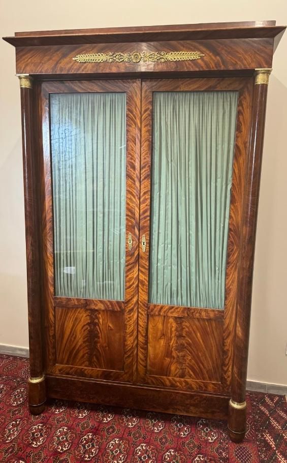 Jolie armoire formant bibliothèque à colonnes détachées, d'époque empire - 19ème,
En placage d'acajou flammé,
Elle ouvre à deux portes vitrées et présente trois étagères intérieure. (vitres avec rideaux plissés vert)
Colonnes détachées de chaque côté avec bague en bronze, décor de palmette sur le haut.
Corniche droite.