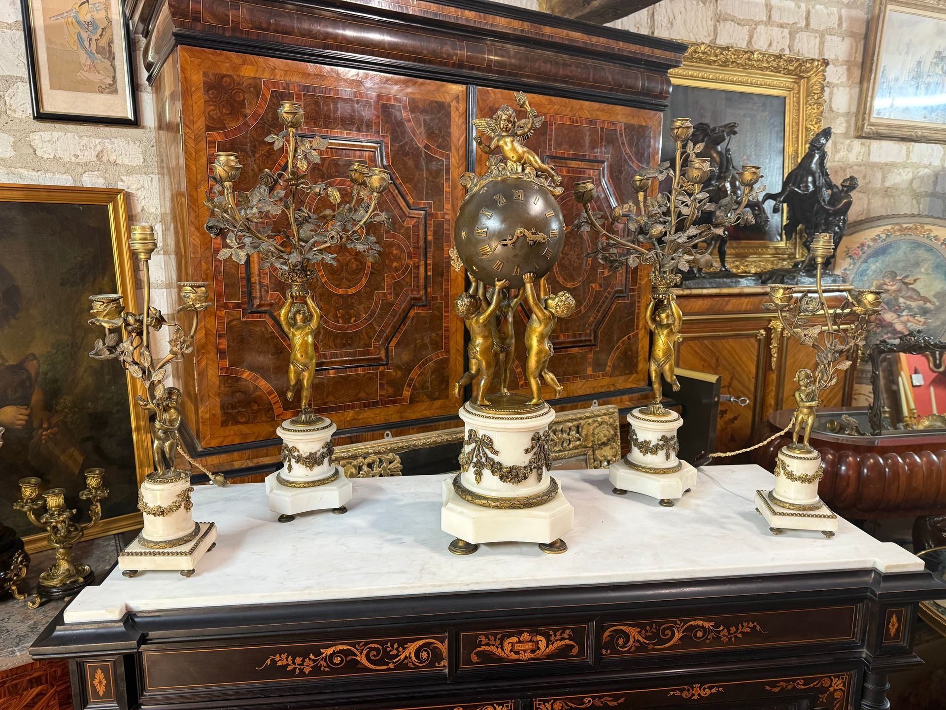 Belle garniture de cheminée de style LOUIS XVI - NAPOLEON III comprenant une pendule et deux paires de candélabres.
- La pendule présente trois putti soutenant un globe céleste en bronze : étoiles, chiffres et aiguilles au lézard en bronze doré.
Le globe est surmonté d’un putti tenant un flambleau.
Le tout sur un socle de marbre blanc en colonne baguée de rais de cœur et ornée d'une guirlande de fleurs et ruban noué en bronze doré et finement ciselé.
- Les candélabres sont à décor d'un putti soutenant des branche de fleurs (des roses) sur socle de marbre blanc identique à ce qui est décrit ci-dessus.
Cette pendule dans son état d'origine nécessite un révision et ses bronzes un nettoyage.
Dimensions : pendule haut 65 prof 22 - petits candelabres haut 46 prof 10 - grand chandelier haut 64 prof 14
