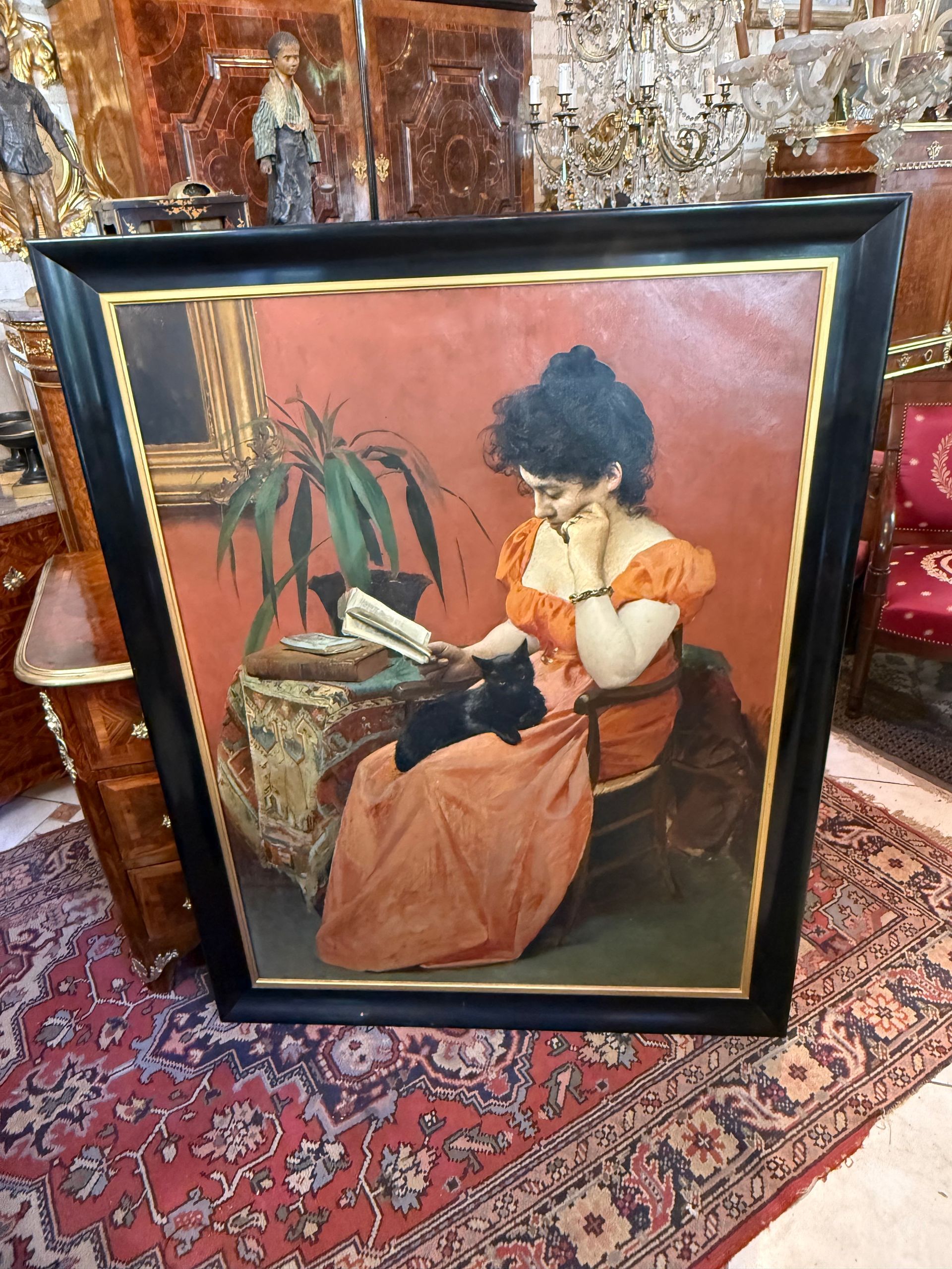 Grande HUILE SUR TOILE fin 19ème représentant une scène d’intérieure soit une femme au chignon assise dans un fauteuil, lisant un livre avec son chat noir sur les genoux. le tout encadré dans un cadre en bois noirci entouré d'un pourtour doré.