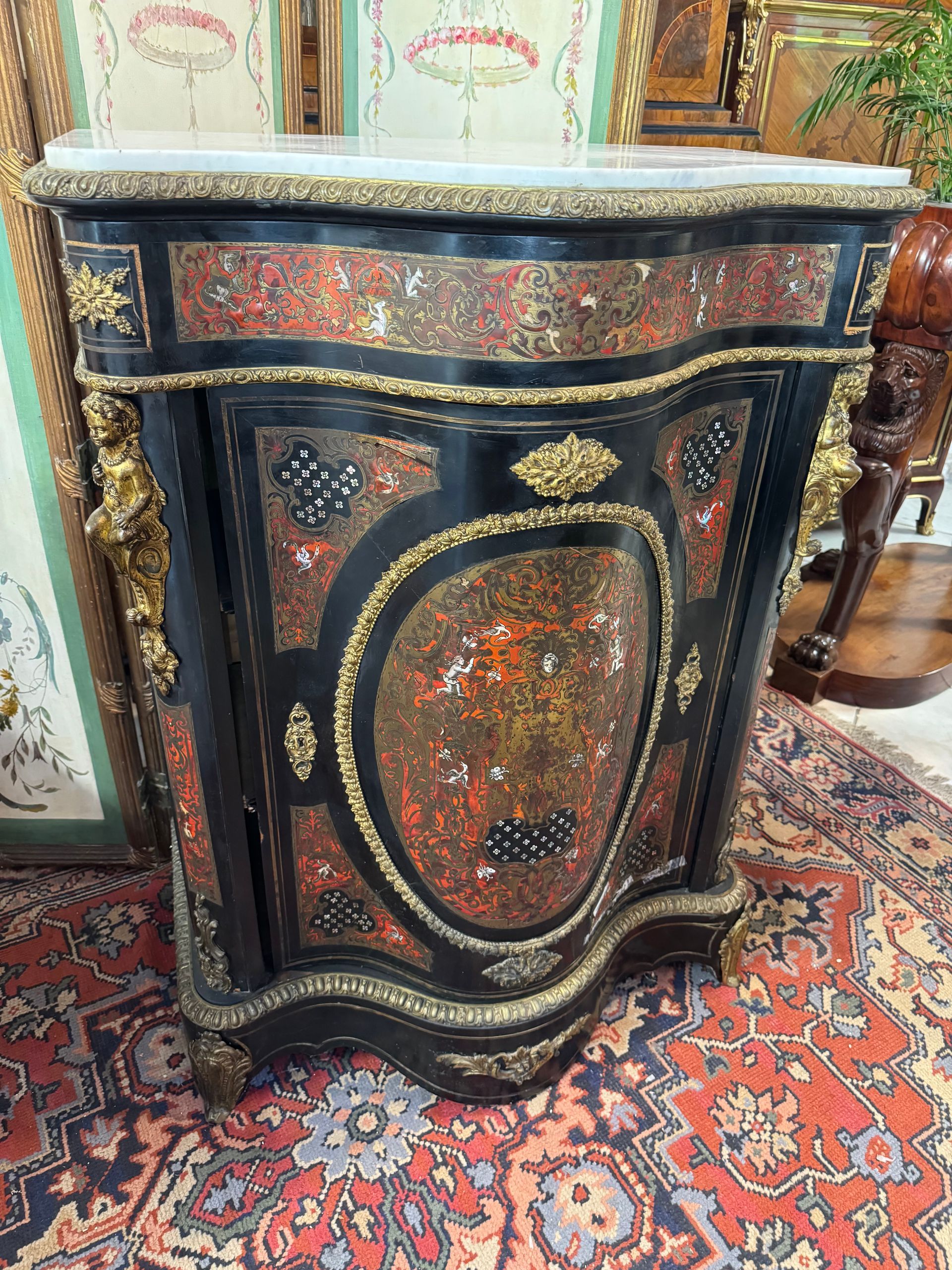 MEUBLE A HAUTEUR D’APPUI BOULLE NAPOLEON III
Meuble à hauteur d’appui, Napoléon III, en marqueterie boulle, bois noirci,  galbé en façade,
Ouvrant à une porte offrant un intérieur avec deux étagères,
Ce meuble présente un décor d’écailles de tortue, filets de laiton et un divers et riche décor de nacre (animaux, écureuils, oiseaux fantastiques, personnages, têtes de personnage,  etc.),
Bronze de tête de chérubins sur les montants
Pourtour de frise en ceinture et dans le bas ainsi qu’une frise formant médaillon sur la façade de la porte.
Le tout coiffé d’un marbre blanc de carrare.