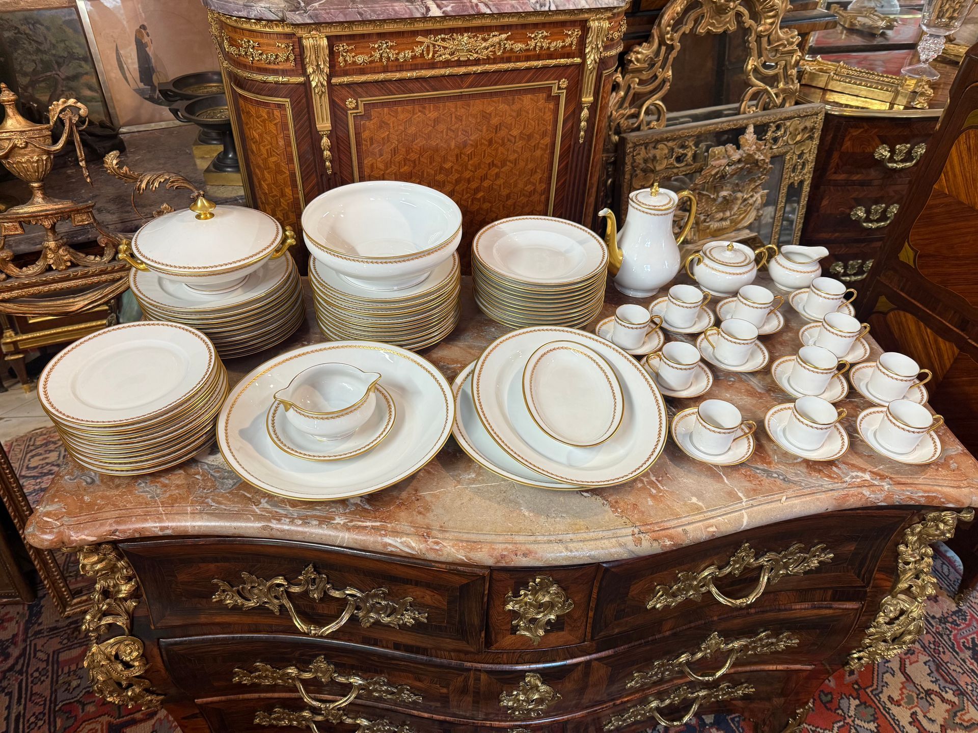 SERVICE DE TABLE HAVILAND LIMOGES fond blanc avec un liseré doré au pourtour et un liseré doré à décor feuillagé intérieur, à savoir : Un service à café en porcelaine comprenant : 1 - Un service à café : douze tasses aves soucoupes, unecafetière, un pot à lait, un sucrier, 2 - Un service de table comprenant : -23 Grandes assiettes Diamètre 24 cm -24 Assiettes creuses Diamètre 23,5 cm -3 Plats, -1 Saladier, -1 Soupière /Légumier avec le couvercle -1 Saucière 1 Raviers A propos de : David haviland : En 1842,David Haviland s’installe à Limoges, la capitale mondiale de la porcelaine etcrée l’atelier Haviland, futur berceau d’un art et dans savoir-faire précieux. Il commença à écrire l’histoire de la famille Haviland , un nom synonyme de l’art du luxe à la française qui perdure jusqu’à aujourd’hui. Négociant, David Haviland crée une entreprise d’importation de faïence et porcelaine en 1838 à New York. En 1842, fasciné par l’or blanc du Limousin, il traverse l’Atlantique pour s’installer à Limoges où il fonde sa propre manufacture. La porcelaine de Limoges prend un essor irréversible et David Haviland est plébiscité par le monde entier pour son œil novateur. Il obtient des récompenses dès 1853 à New York, une médaille d’or à l’Exposition du Crystal Palace, puis le gouvernement français salue son talent, en lui décernant une médaille d’argent à l’Exposition Universelle de Paris en 1855.