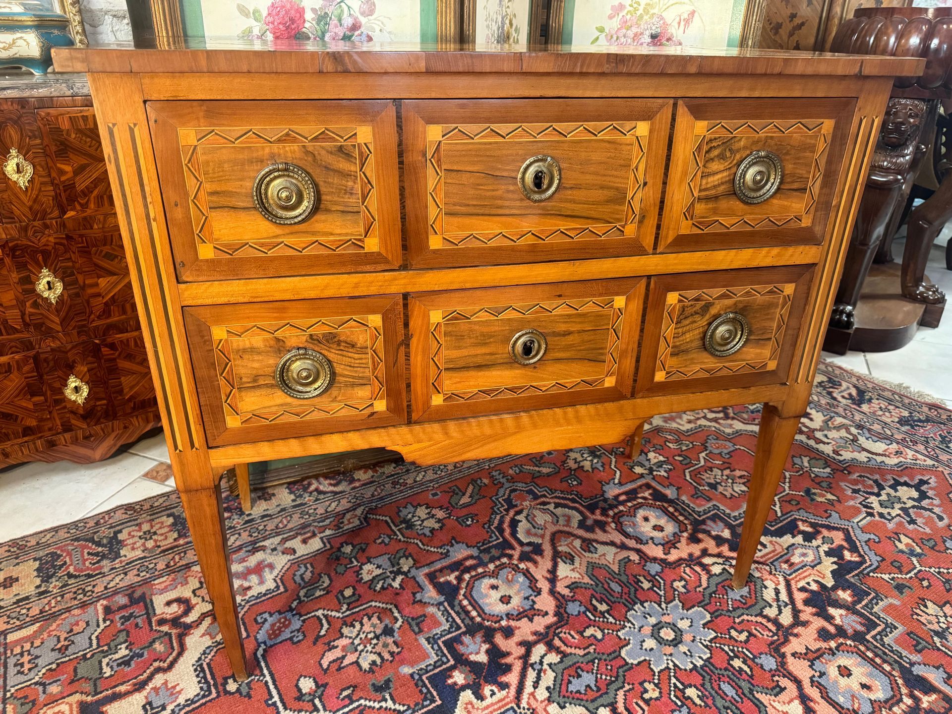 Elégante commode dite sauteuse  d'époque Louis XVI - XVIIIe siècle, ouvrant à deux tiroirs et reposant sur des pieds fuselés.
Elle est en noyer massif et placage de noyer, structure en sapin.
Elle  présente un riche décor à motif de losanges et filets verts.
Poignées de tirage en anneaux. Possède sa clé.