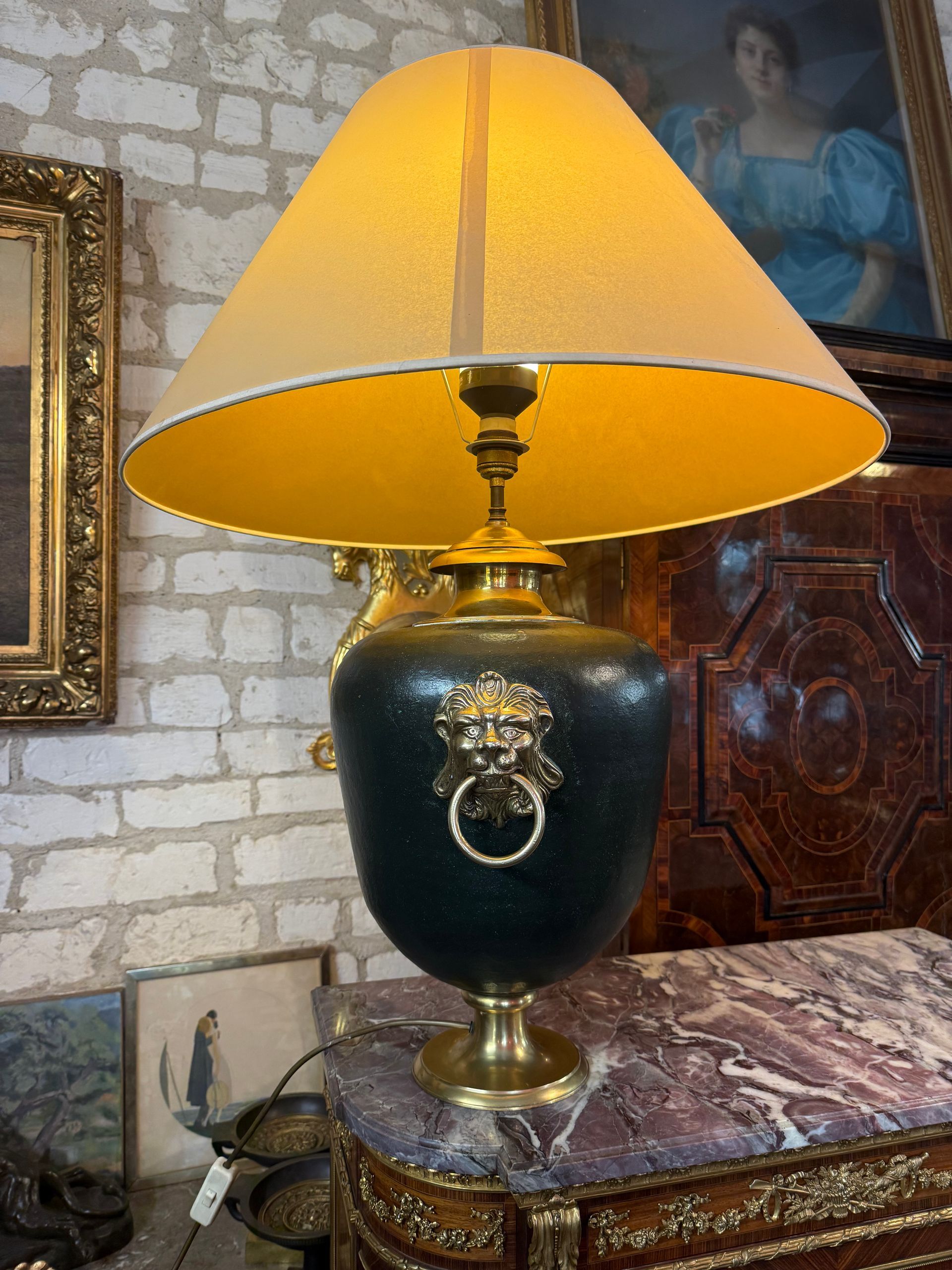 Lampe de salon anglaise, sur piedouche, vase de forme ovoïde de couleur verte, Anneau avec tête de lion, formant heurtoir en laiton pour une prise en mains de chaque côté, Abat-jour de couleur jaune, Lampe électifriée en état de fonctionnement. Dimensions : Lampe seule 50 cm avec l'abat-jour 90cm Profondeur 30cm