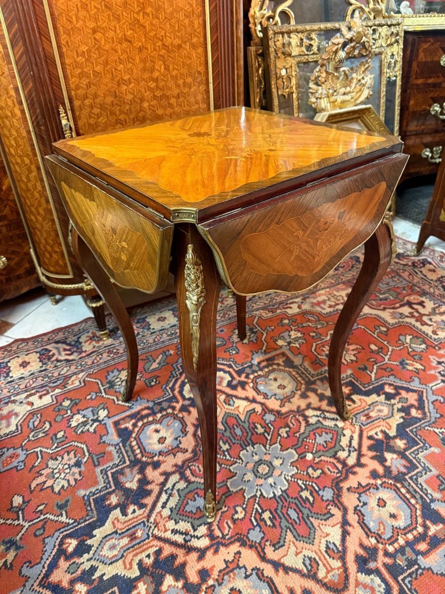 Table à jeux dite « mouchoir » à quatre feuilles de style Louis XV – 19ème en placage de bois de rose, palissandre et bois teinté, marqueterie à décor floral sur le plateau de fome carrée et les quatre feuilles, Ouvrant par quatre abattants repliables, Le tout reposant sur des pieds cambrés avec un décor de chutes en bronze sur les montants et les sabots.