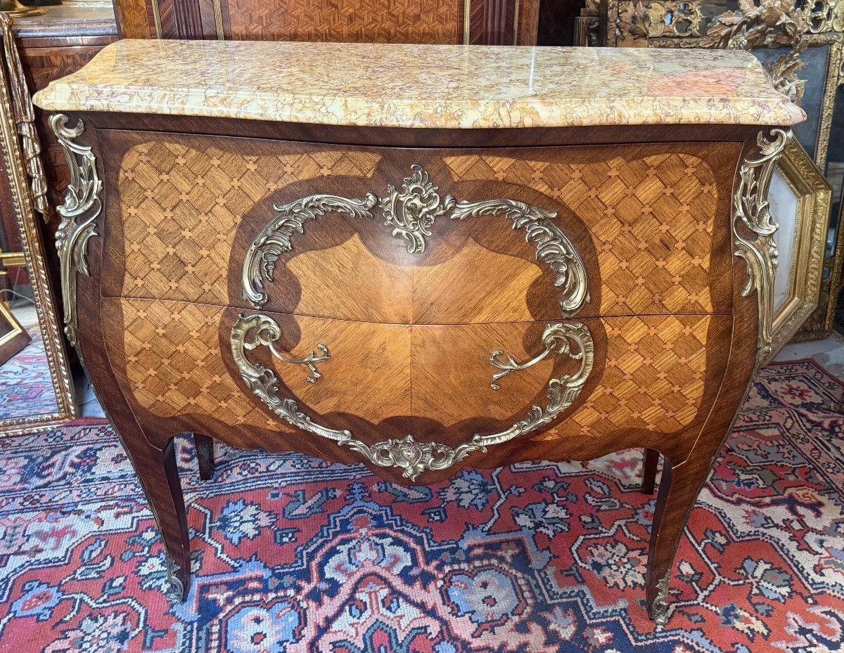 Commode dite sauteuse de style Louis XV En placage de bois de rose et de palissandre, marqueterie à la reine en façade et sur les côtés, Commode galbée toutes faces, offrant une garniture de bronze doré ciselé, Dessus coiffé d'un marbre à gorge jaune veiné. Travail du Faubourg Saint Antoine à Paris des années 1950.