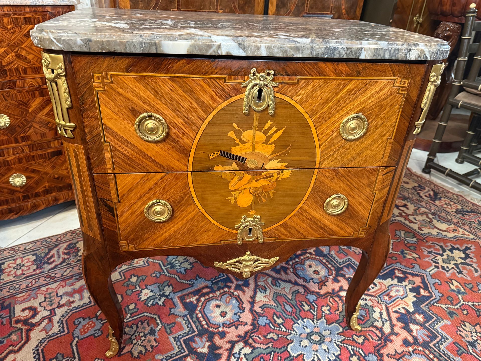 Petite commode dite « sauteuse « Louis XV transition, XVIIIème,  en bois de placage, bois de rose en frisage et amarante,
Cette commode de forme rectangulaire ouvre à deux tiroirs à traverse dissimulée, avec poignées en anneaux tombants,
La façade offre un décor représentant un médaillon central avec attributs de musique,  filets à la grecque dans un entourage d’amarante,
Garniture de bronze doré et ciselé,
Les montants sont droits,
Le tout reposant sur des pieds cambrés se terminant par des sabots,
Elle est coiffée d’un marbre  brèche à congé gris-noir moucheté.
Estampillé J. DUBOIS.
A propos de :  Jacques Dubois (1693-1763) - ébéniste - Maître le 5 septembre 1742. Dubois est un grand maître, qui a su ne pas se confiner dans un genre et qui a su adapter son talent souple et varié à tout ce qui dans le mobilier, pouvait représenter la beauté et la noblesse des lignes.