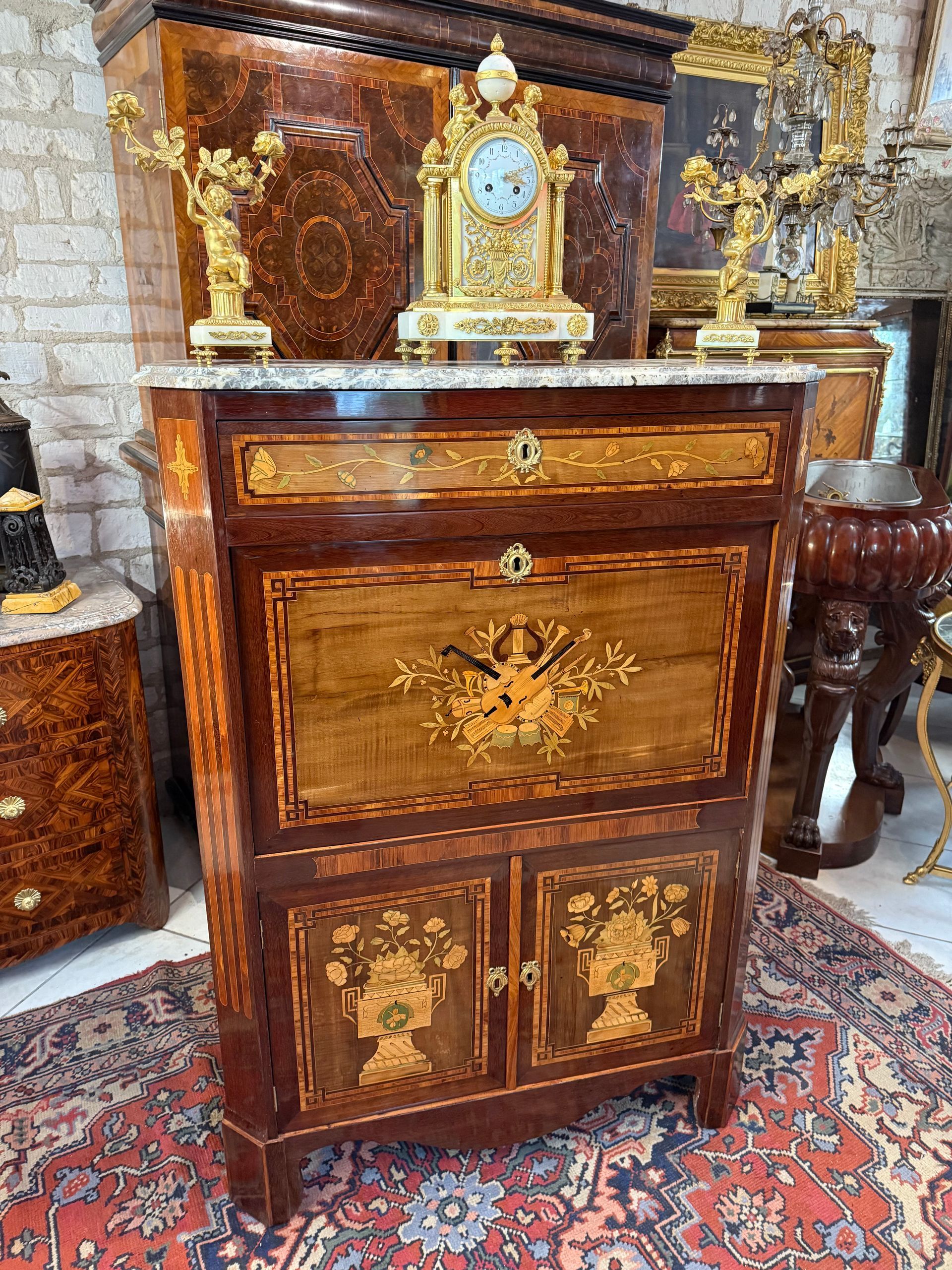 Elégant secrétaire d’apparat époque Louis XV – TRANSITION, 18ème,
En placage d’amarante, bois rose dans les encadrements,  citronnier et bois teinté,
Vernis au tampon.
Il présente :
→ en façade dans la partie haute sur l’abattant un décor aux attributs de la musique , dans la partie basse sur chaque porte un décor de cassolettes de fleurs ,
→ sur chaque côté un riche décor floral.
Il ouvre par :
→ Un abattant ou l’on découvre un intérieur composé d’une étagère, deux casiers, six petits tiroirs soit trois de chaque côté séparé par un casier et une table d’écriture-bureau recouverte d’un cuir noir d’origine,
→ Dans la partie basse ouvrant à deux portes un intérieur composé deux tablettes dont une compartimentée en deux.
Les montants sont à pans coupés.
Le tout coiffé d’un marbre d’Alep gris-blanc.
A Noter une trace d’estampille JE sur le montant du haut.
Beau travail parisien du 18ème.