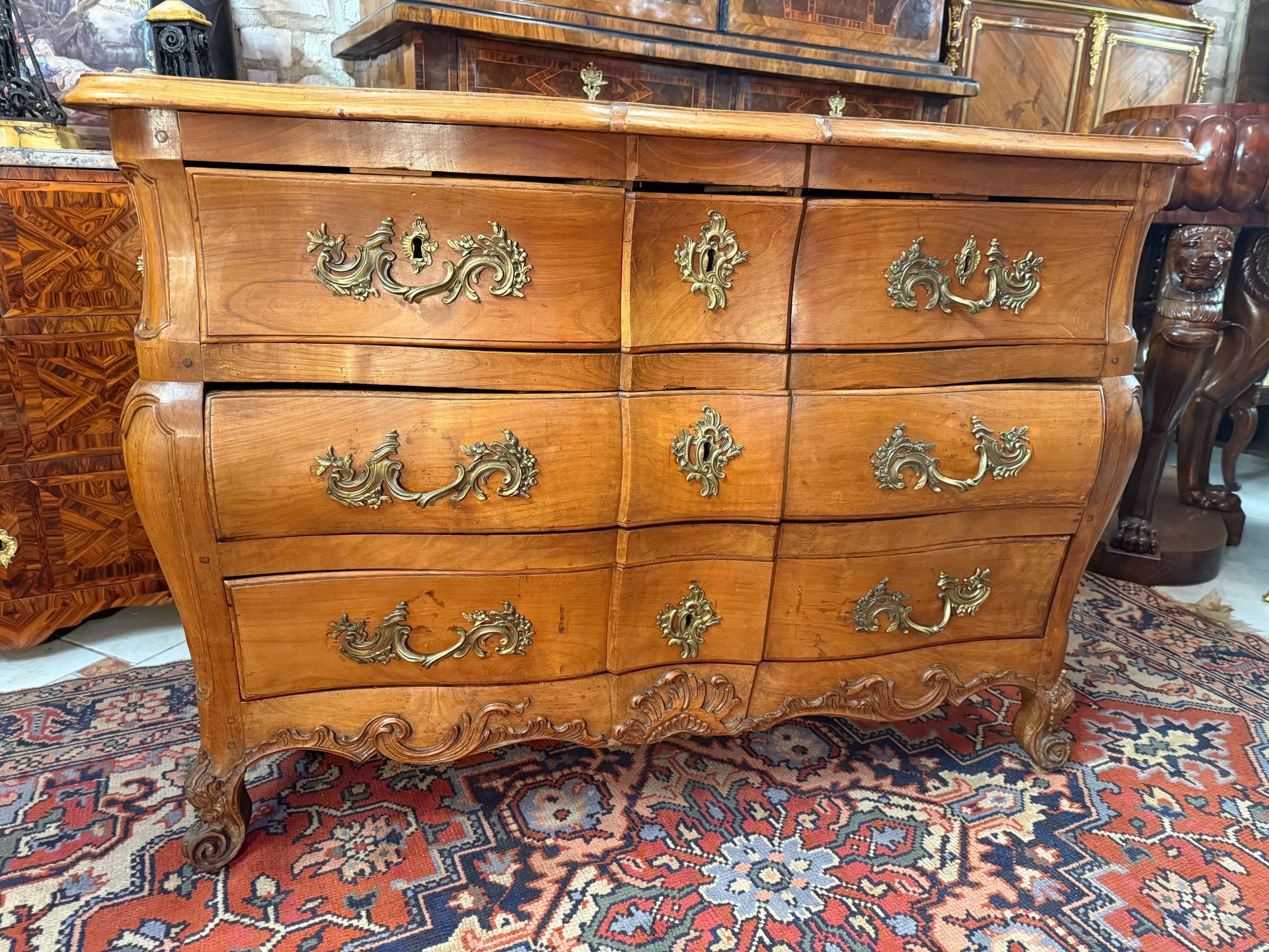 Commode de forme tombeau d'époque LOUIS XV – 18ème siècle ,  en merisier massif , galbée en façade,  ouvrant à cinq tiroirs sur trois rangées,
L'ensemble est richement orné de bronzes dorés et ciselés sur les entrées de serrure, et les poignets de tirage , anciennes et d'origine.
Elle repose sur pieds sculptés à enroulement. 
bandeau sculpté dans le bas, 
Plateau bois marqueté.
Travail du Sud-Ouest de la France.