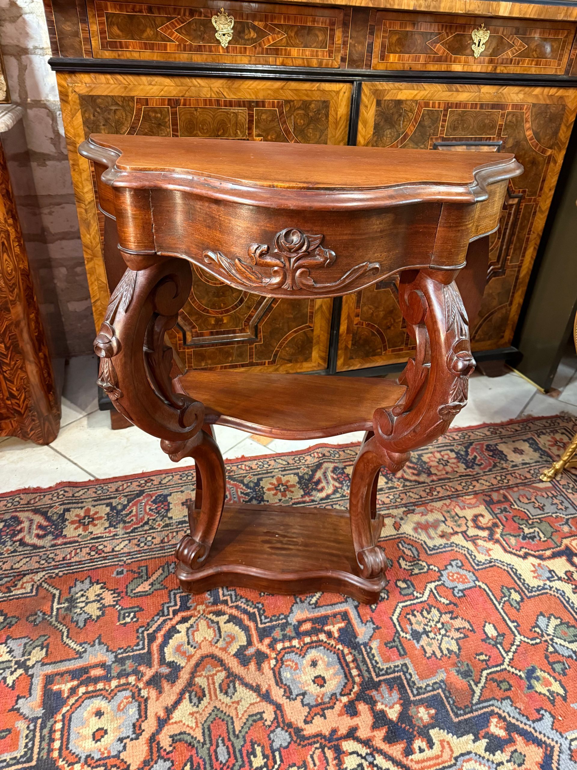 Petite console de style Louis Philippe en acajou, à plateau chantourné,
Cette console ouvre à un tiroir en ceinture et repose sur deux pieds antérieurs dont les montants avants sont à cross vers le haut.
Le tiroir et les pieds sont sculptés à décor de fleurettes.
Cette console est reliée par un plateau tablette d’entretoise dans son milieu et repose sur un  socle.