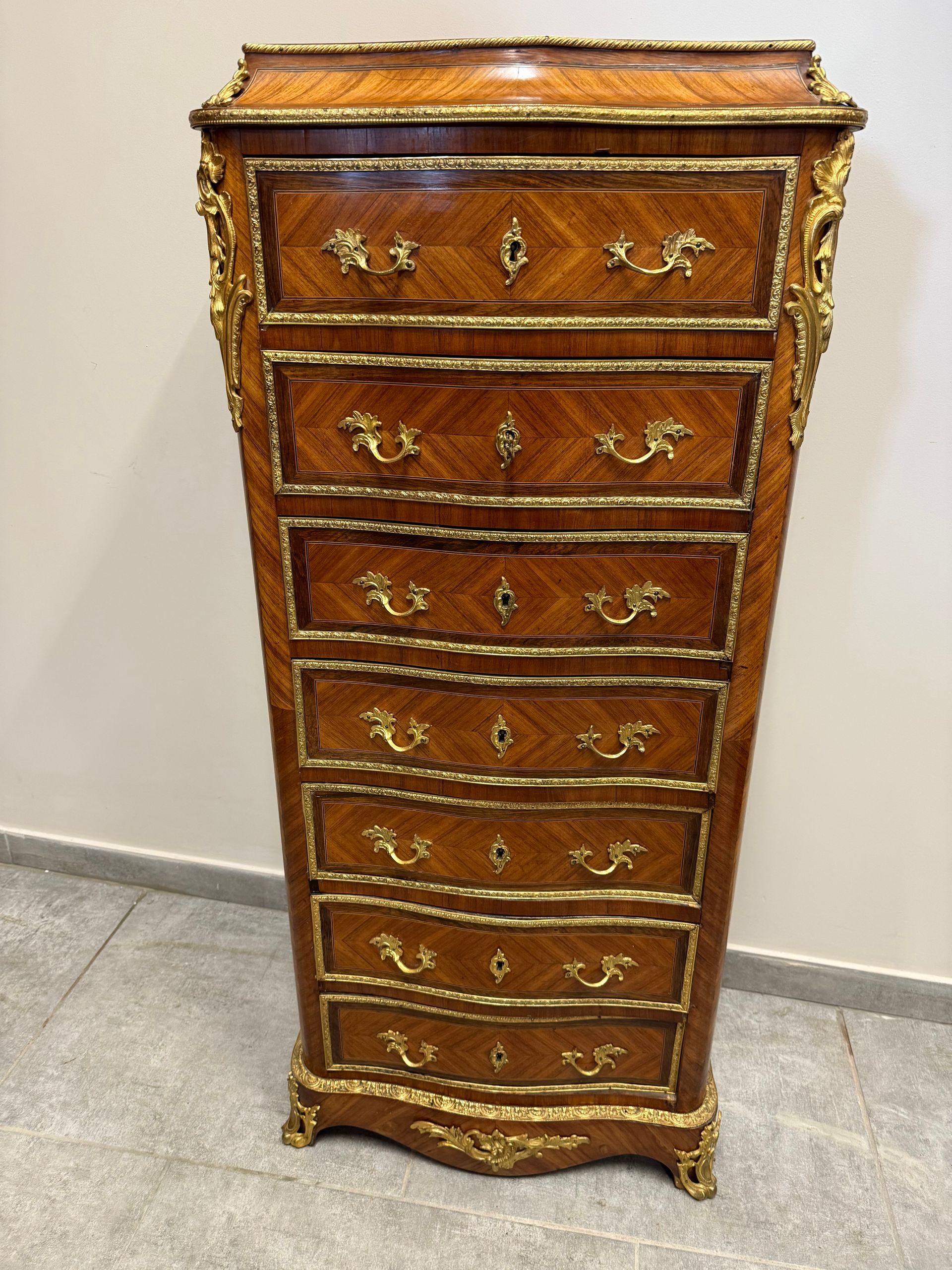 Semainier de forme mouvementé de style Louis XV, époque Napoléon III, en bois de placage et marqueterie de bois de rose et pallisandre,
ouvrant par sept tiroirs, avec poignées de tirage feuillagé, entourage d'une frise de laiton sur chacun des tiroirs, chutes de bronze finement cislé sur les montant et sur la traverse du bas.
Sur dessus, marqueterie de damier formont losange,