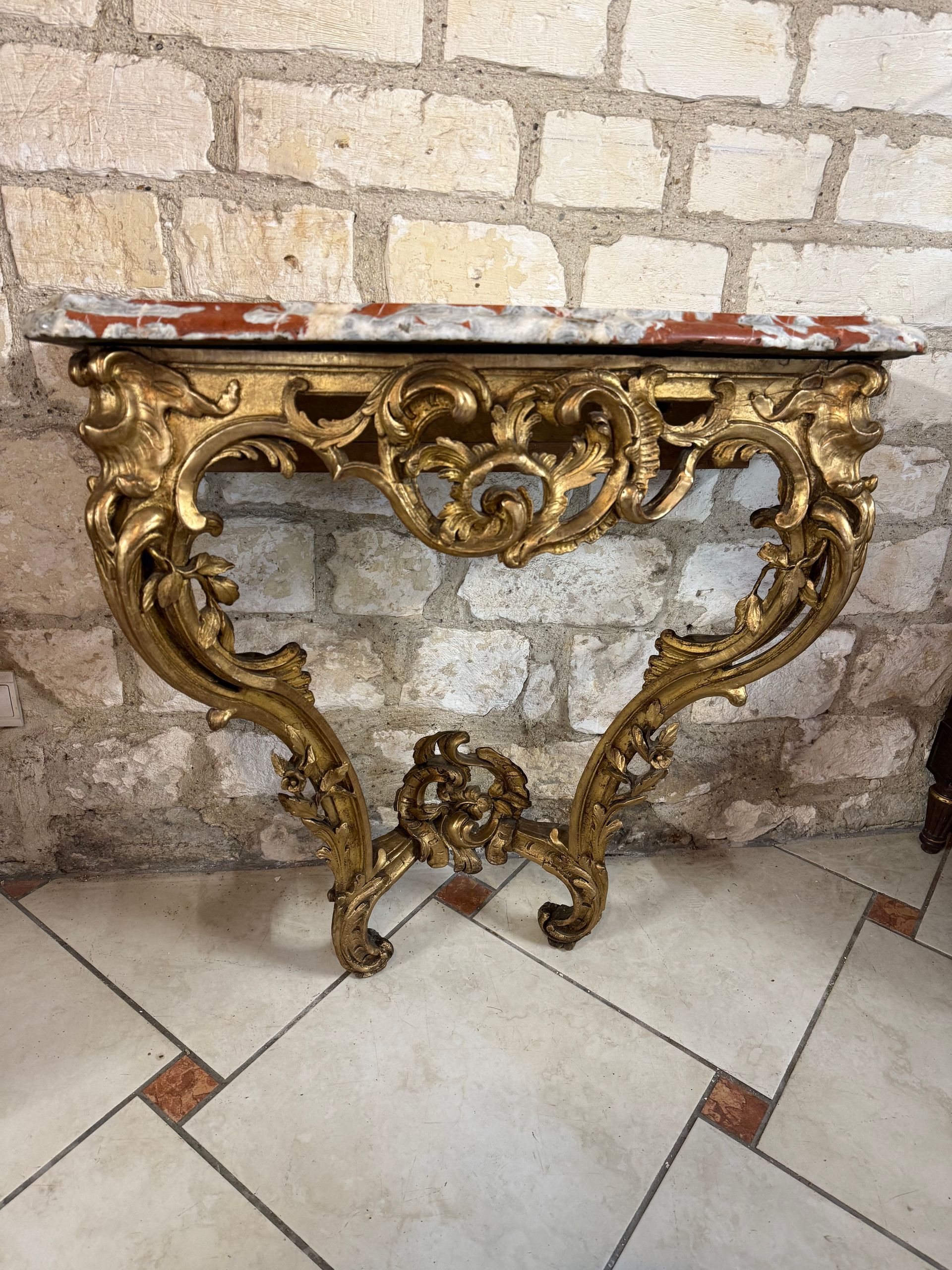 Console d’applique d’époque Louis XV- 18ème en bois sculpté et doré, à décor de feuilles d’acanthe, feuillages et fleurs dans son ensemble,
Elle repose sur deux pieds en chien de fusil reliés par une entretoise surmontée d’une feuille d’acanthe ajourée et stylisée.
La traverse haute est ajourée et entrelacée de feuilles d’acanthe, centrée par une coquille dans son milieu
Le tout coiffé d’un épais marbre brèche veiné rouge de 4cm.