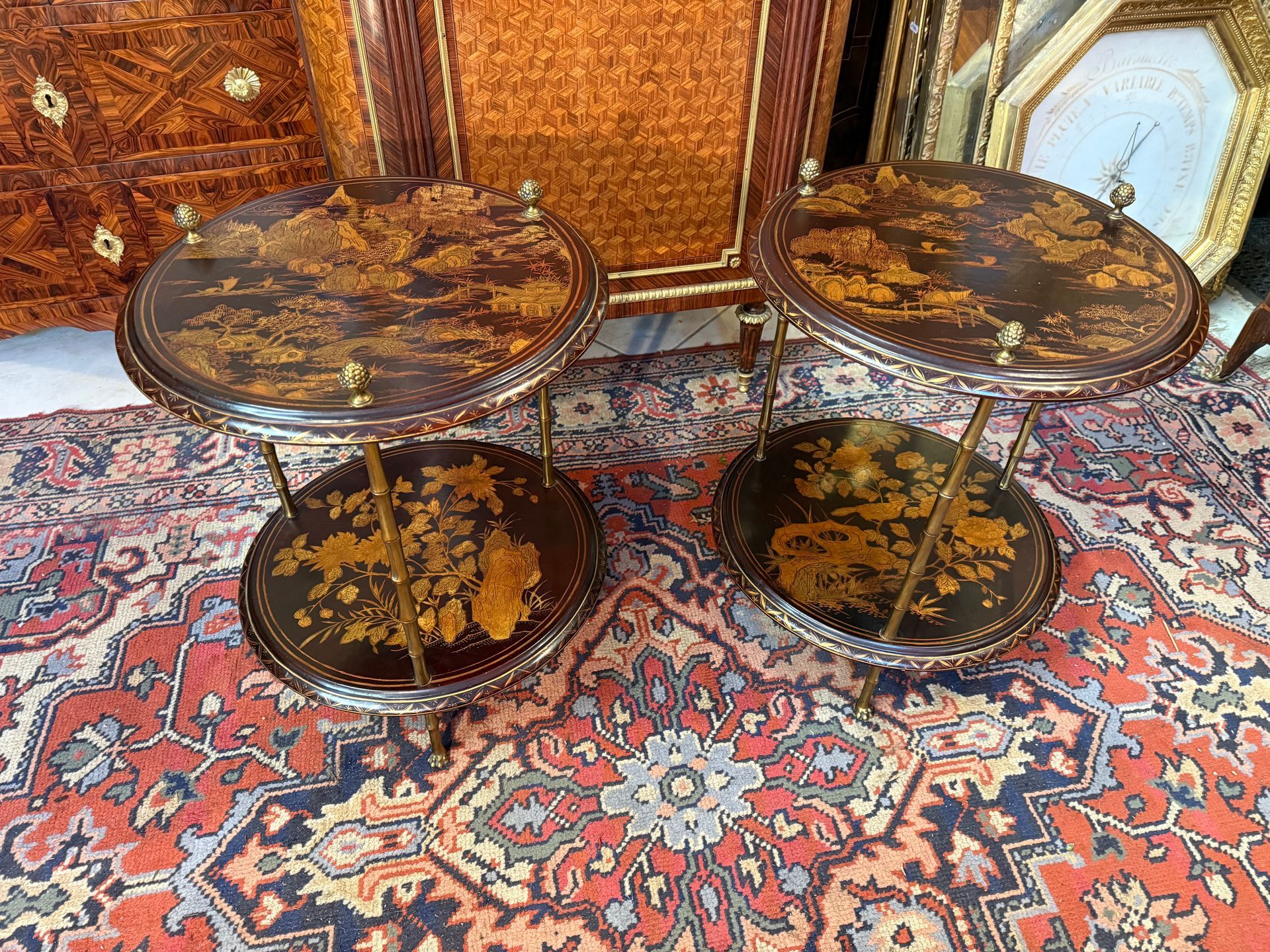 Paire de bout de canapé de forme circulaire en bronze doré et laque de chine à deux plateaux superposés à  décor chine soit :  fleurs, végétaux , oiseaux et paysages colorés sur fond noir. Piètement de forme bambou se terminant par des pieds griffes et surmonté de pommes de pin MAISONS BAGUES 1960
