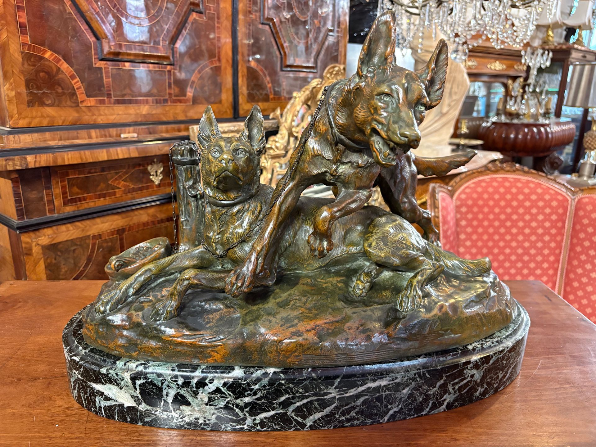 Sculpture française de deux chiens, R Varnier pour le Salondes Beaux-Arts 1923, sur spcle en marbre noir moucheté, Bronze à patine brune représentant deux bergers enchainés à un poteau, avec la gamelle à nourriture sur le côté, L'un d'eux est couché, le visage alerte et les oreillesdressées et en avant, tandis que l'autre s'élance à moitié sur son partenaire,une jambe en l'air, la bouche ouverte et les oreilles en avant Signé R. Varnier sur labase arrière du bronze et portant  la mention «Salon des Beaux-Arts 1923» et le cachet de l’éditeur «Patrouilleau Edit. PARIS»