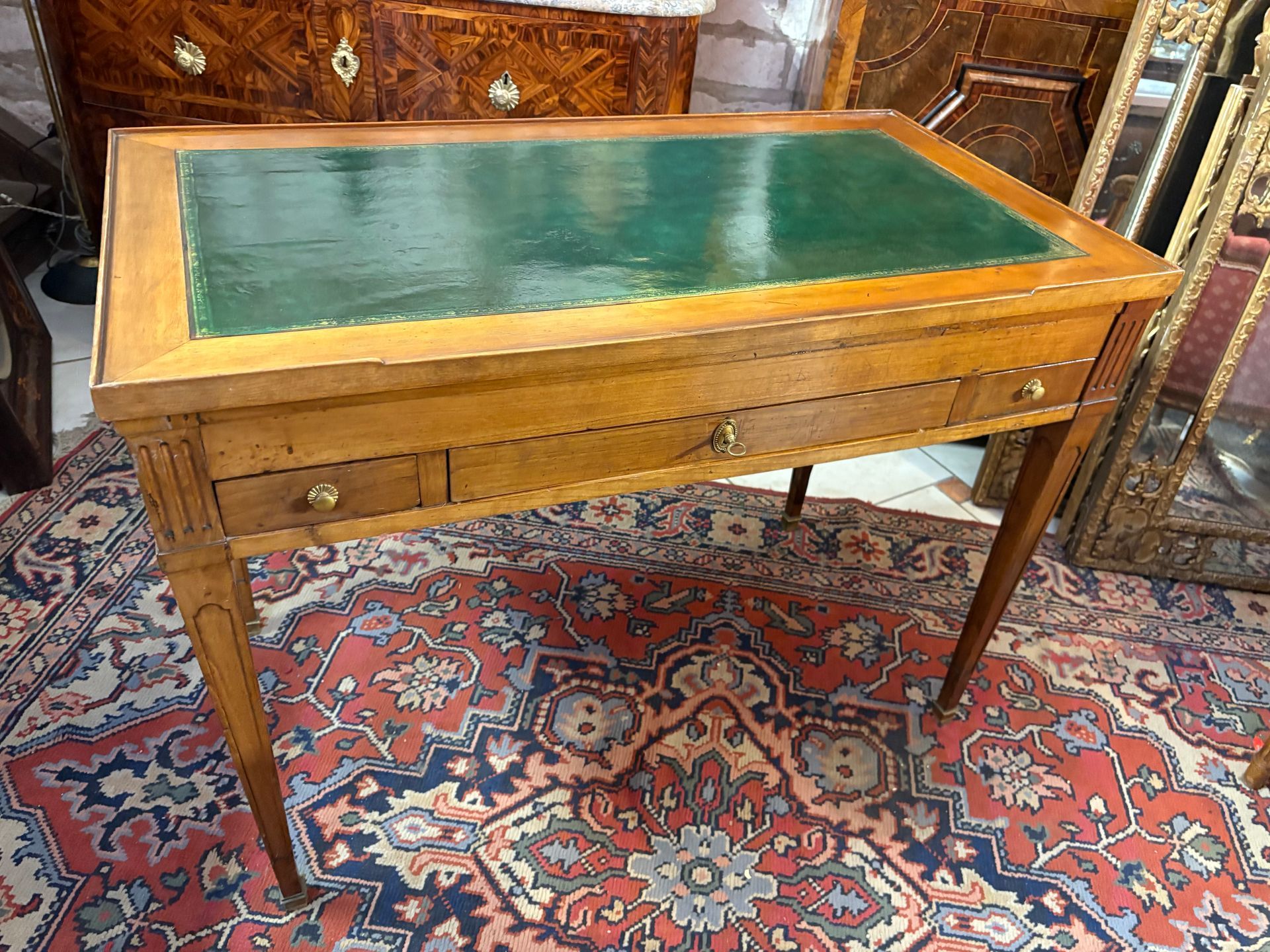 Table Tric Trac, époque Louis XVI - 18ème en cerisier  Elle ouvre à trois tiroirs et repose sur quatre pieds fuselés, cannelures dansles angles,  terminés par des sabots enbronze doré. Plateau amovible  gainé de cuir vert avec un liseré doré petites feuilles (étatd’usage)  d’un côté et feutre vert de l'autre. Caisson découvrant à l’ intérieur un  jeu de jacquet.