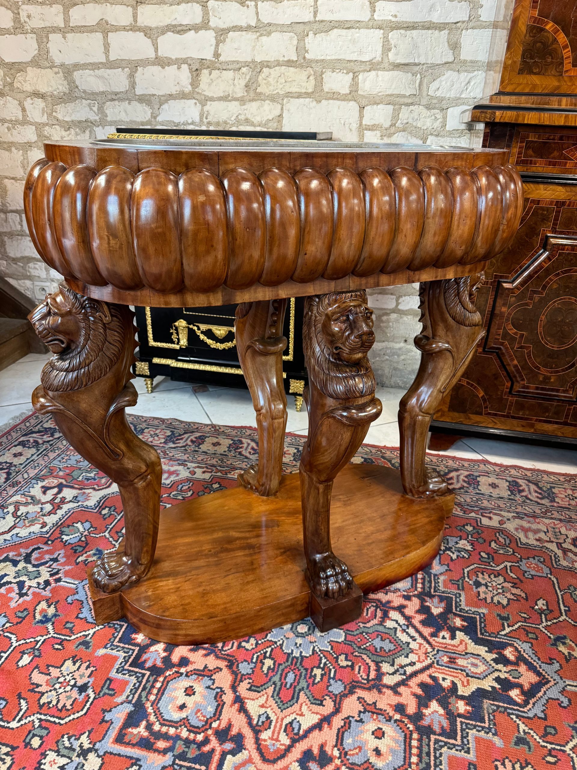 Importante Jardinière (de belles dimensions), époque Empire, en acajou massif et  placage d'acajou, vernis au tampon, structure en chêne.
De forme ovale avec de larges et épais godrons, avec son intérieur en zinc amovible,
Soutenue par quatre patères sculptées formant un décor de lions dressés sur leurs pattes (acajou massif), (hauteur des lions 72 cm),
Le tout reposant sur un socle épais de 8,5cm.
Travail anglais du début 19ème.