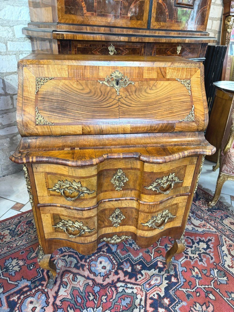 Petite commode scribanne en noyer de style Louis XV . époque 19ème,
galbée en façade avec une jolie garniture de bronze dans son ensemble.
Elle ouvre :
- par un abattant découvrant un aménagement de cinq petits tiroirs, une niche.
- la partie commode ouvre à deux tiroirs,
Le tout repose sur quatre pieds cambrés.