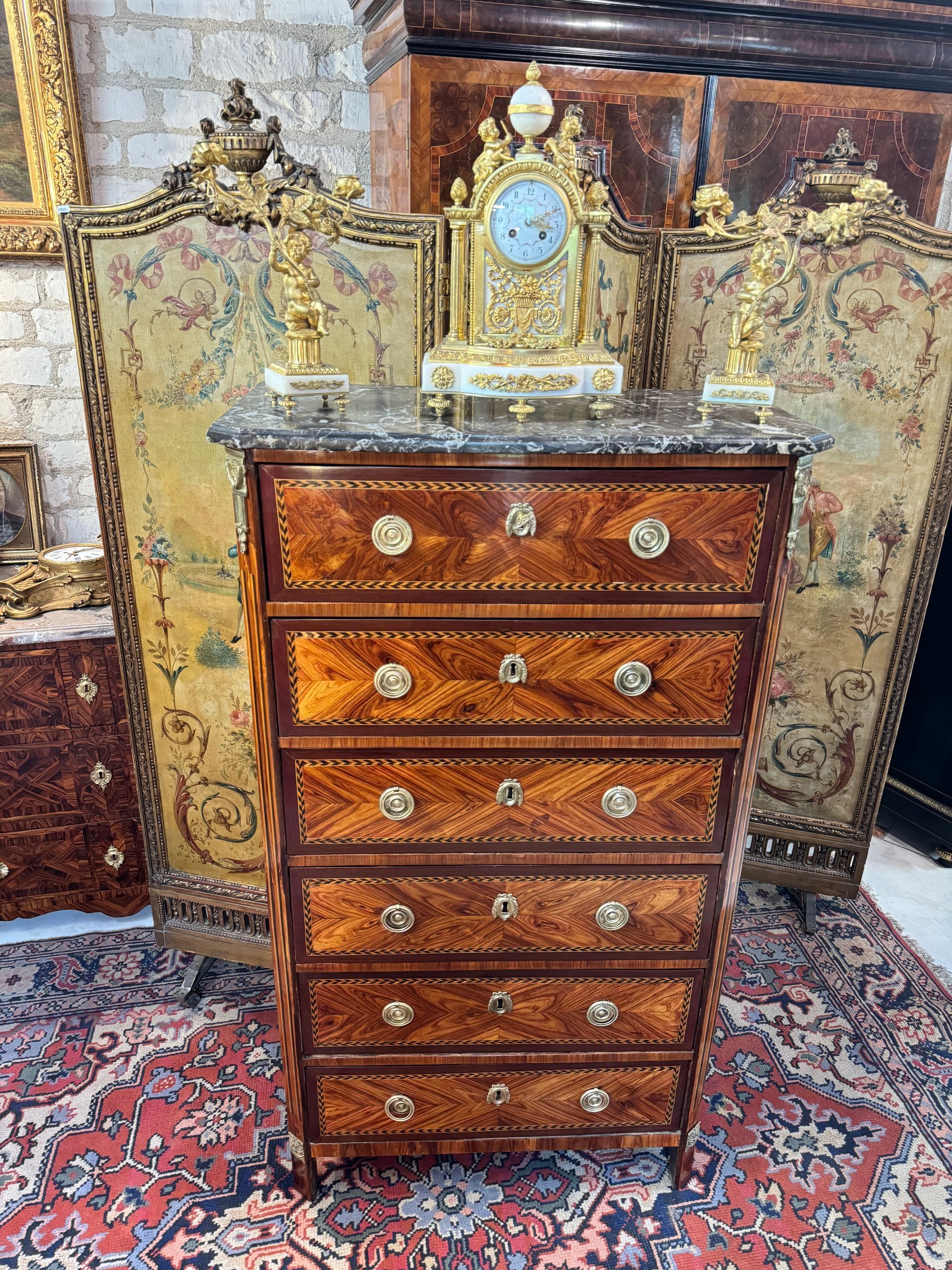 Chiffonnier en placage de bois de rose, encadrement d'amarante, entourés de filets à la grecque, XVIIIème, époque Louis XVI,
Vernis au tampon.
Il ouvre à six tiroirs, 
Montants à pans coupés terminés par des pieds droits. chute de bronze.
Dessus de marbre gris Sainte Anne (à noter une restauration anncienne sur le dessus de ce marbre)
Estampille Nicolas PETIT
Légende : Nicolas Petit  passé Maître en  1761 tenait son atelier