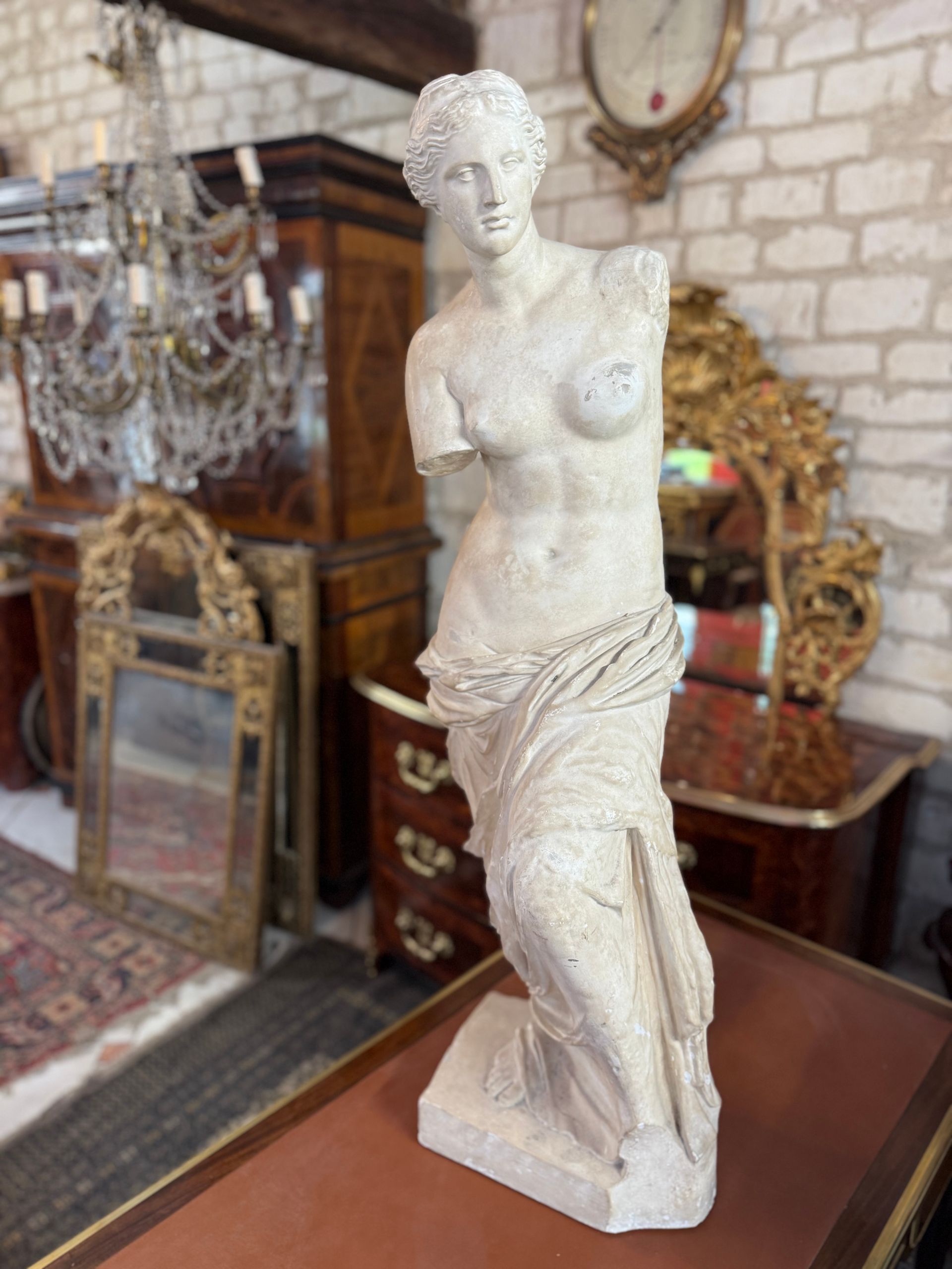 Statue représentant la Venus De Milo,  
Sculpture en platre de belle hauteur. A noter un petit éclat au niveau d'un sein.  
La sculpture originale (musée du Louvre. 130-120av. J.-C.) a été découverte sur l’île de Milos en 1820 et est une piècesculptée au IIe siècle av. J.-C., basée sur un original de l’école athéniennede Praxitèle du Ve siècle av. J.-C. Elle est considérée comme le prototype del’image de la beauté du monde classique.