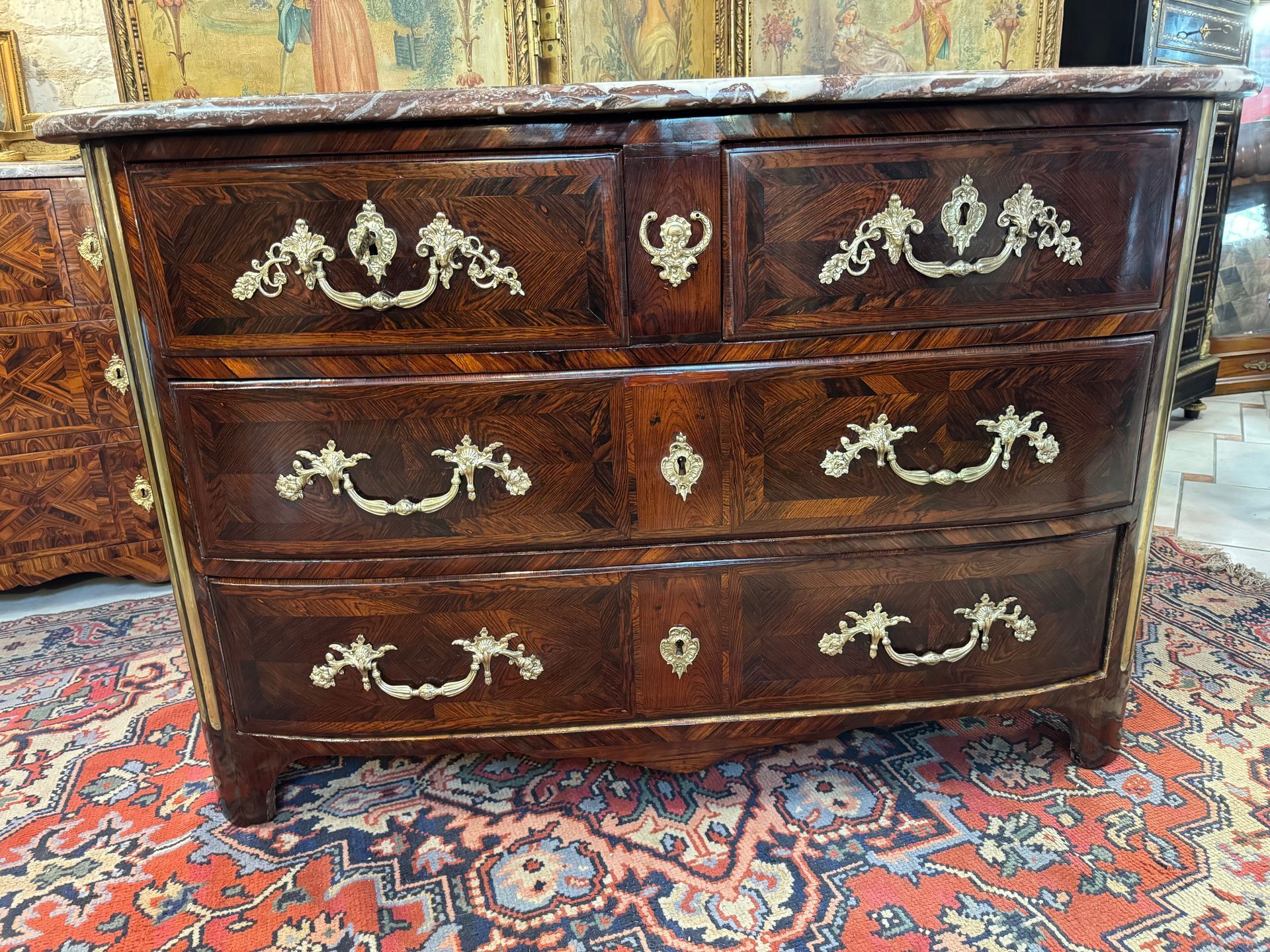 Commode 18ème époque  Louis XIV ,
Commode Louis XIV de forme cintrée , d'époque XVIIIe Siècle .
Elle est en placage de palissandre et vernis au tampon,
Léger ressaut sur les côtés.
Elle ouvre en façade par quatre tiroirs sur trois rangées , dont deux plus petits dans la ceinture ,
Elle offre  des poignées tombantes en bronze doré d’origine .  
Les montants sont arrondis ornés de cannelures en laiton
Le tout coiffé d’un marbre brèche .