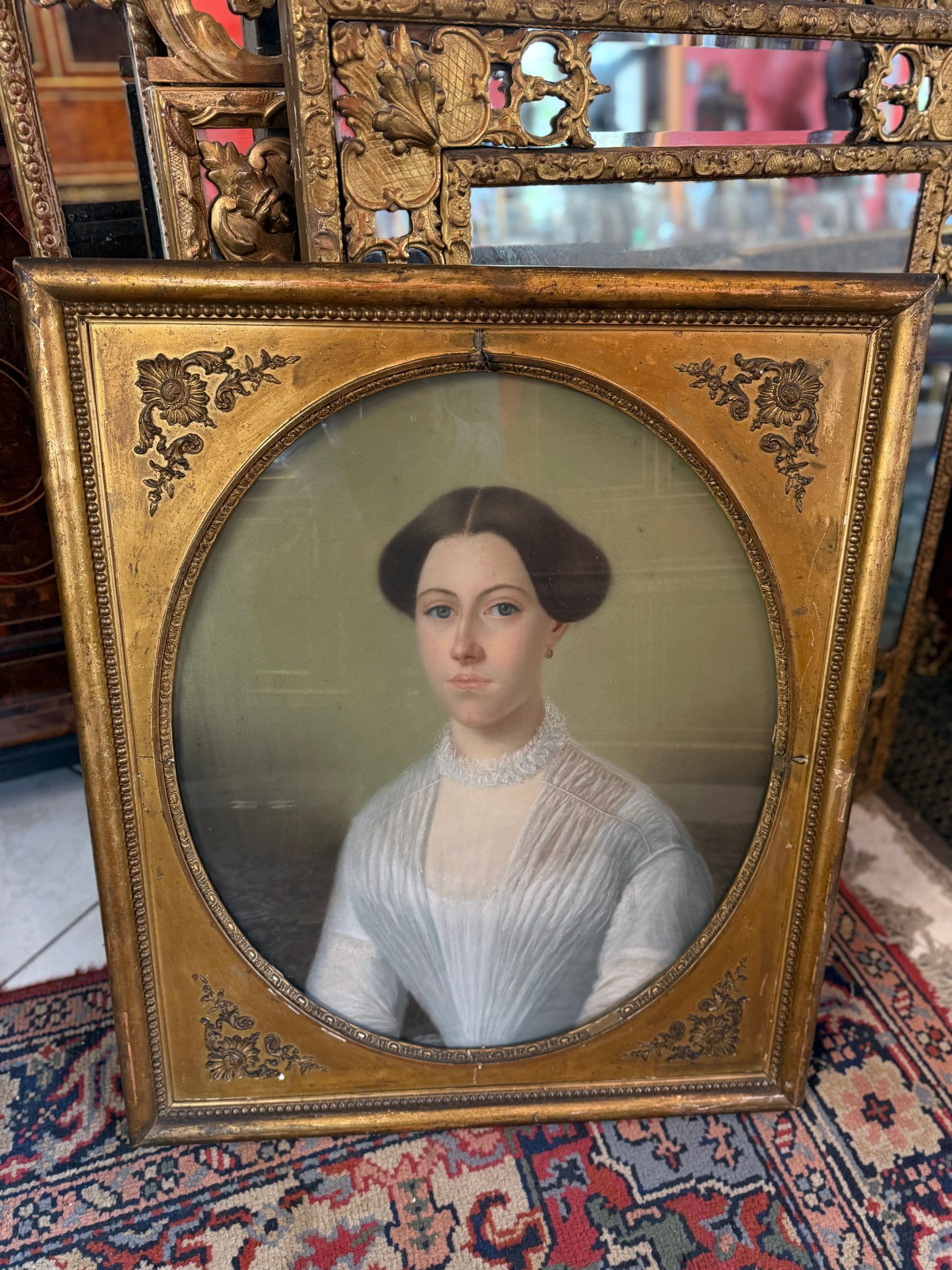 PASTEL à vue ovale, représentant le portrait d'une femme élégamment vêtue d'une robe blanche, au visage fin, regard intense. Ce pastel est mis en valeur dans un cadre doré en bois stuqué. Daté sur le coté gauche : 1852