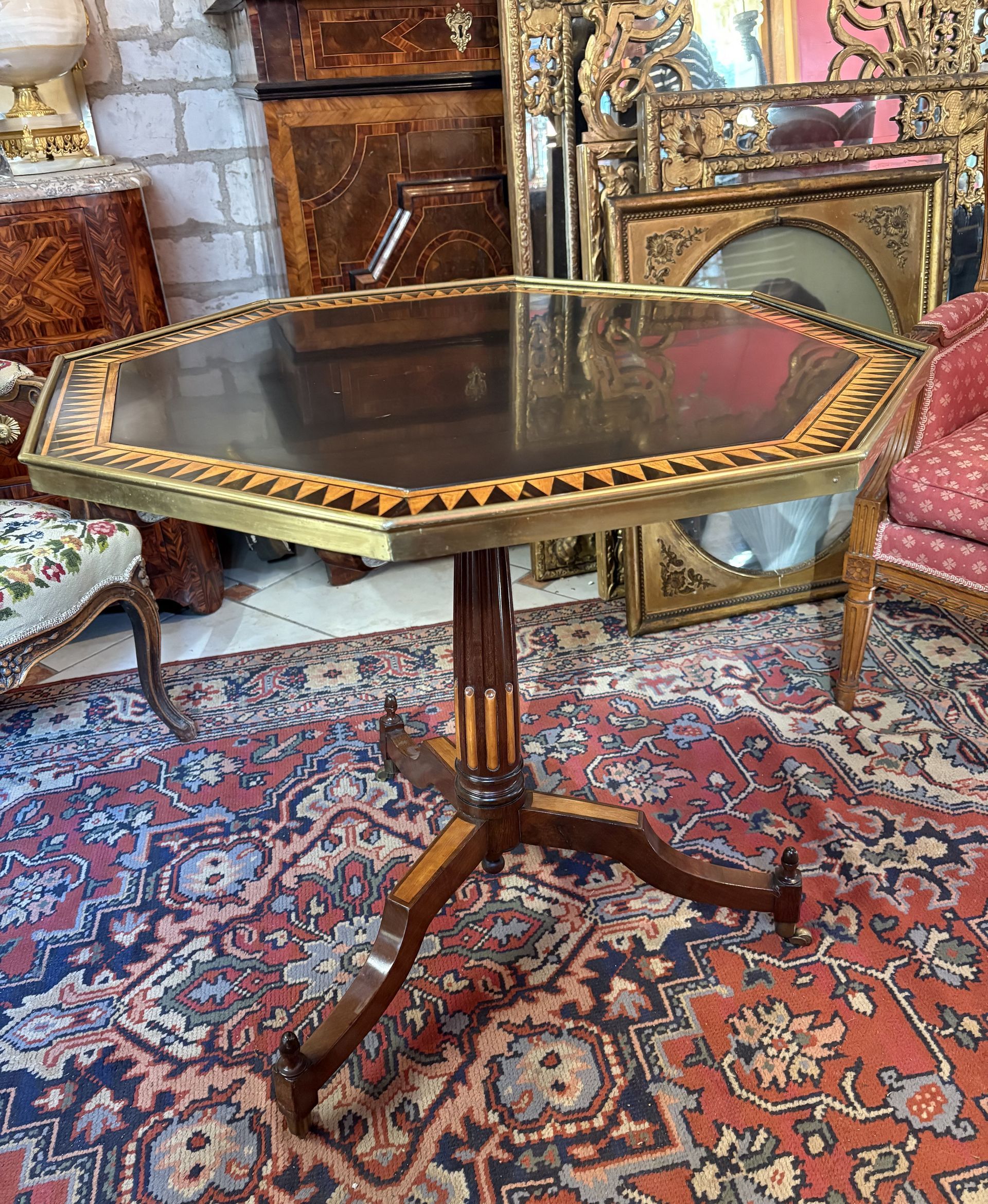 Guéridon de forme octogonale  en acajou et placage d'acajou, bois de citronnier et d'ébène fin XVlll  joli décor sur le plateau marqueté de dents de loups centré d'un marbre noir, galerie en laiton  Facile de déplacement  pieds tripodes sur roulettes surmontés d'un fût cannelé et rudenté. Le plateau octogonal basculant.