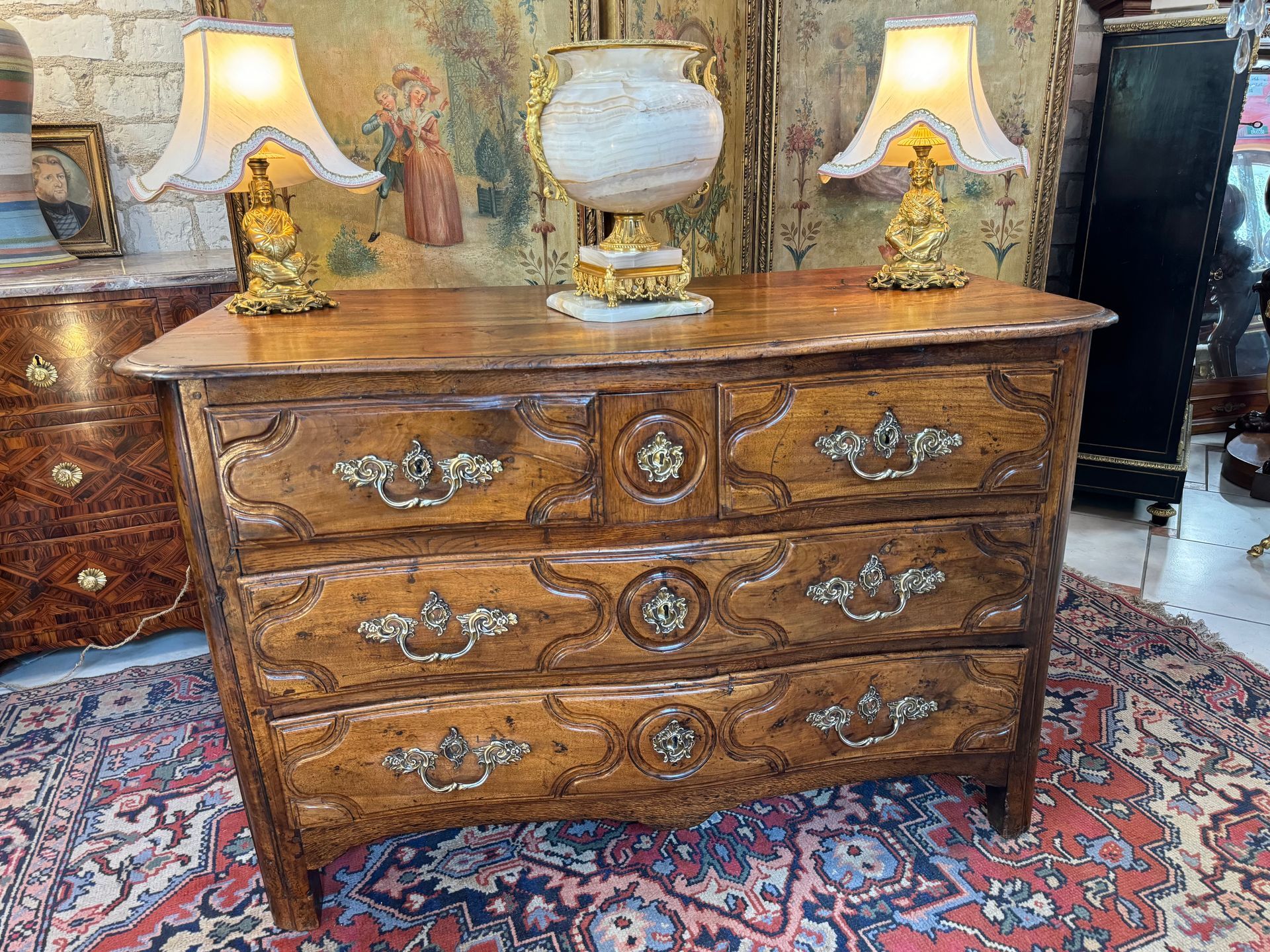 Commode île de France dite parisienne louis XIV - XVIIIème en noyer,
Cette commode est galbée et ouvre par cinq tiroirs (dont un tiroir secret) sur trois rangées aves des poignées de tirage en bronze doré, Les serrures sont d'origine, possède sa clé.
Les côtés sont moulurés;
Elle repose sur des pieds droits,
Le tout coiffé d'un plateau bois.