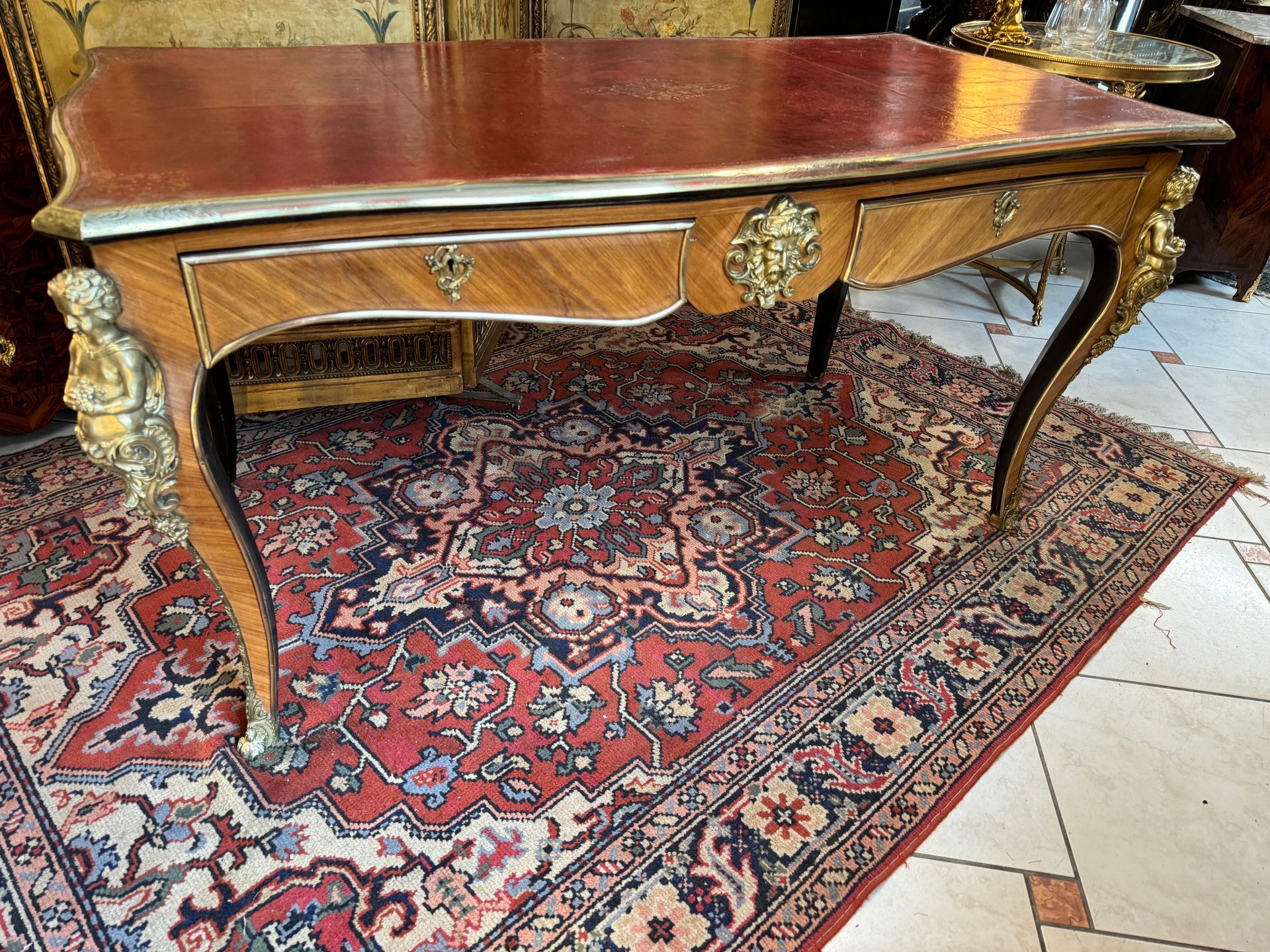 Bureau plat de style Louis XV - 19ème siècle, double face, en placage de Palisandre , 
Ornementation de bronze doré et chutes de chérubins à chaque angle,
Ouvrant à deux tiroirs, entrée de serrure représentant un faune,
Pieds cambrés se terminant par des sabots ,
Lingotière en laiton et  plateau recouvert d’un cuir bordeau et vignette dorée. Meuble très décoratif