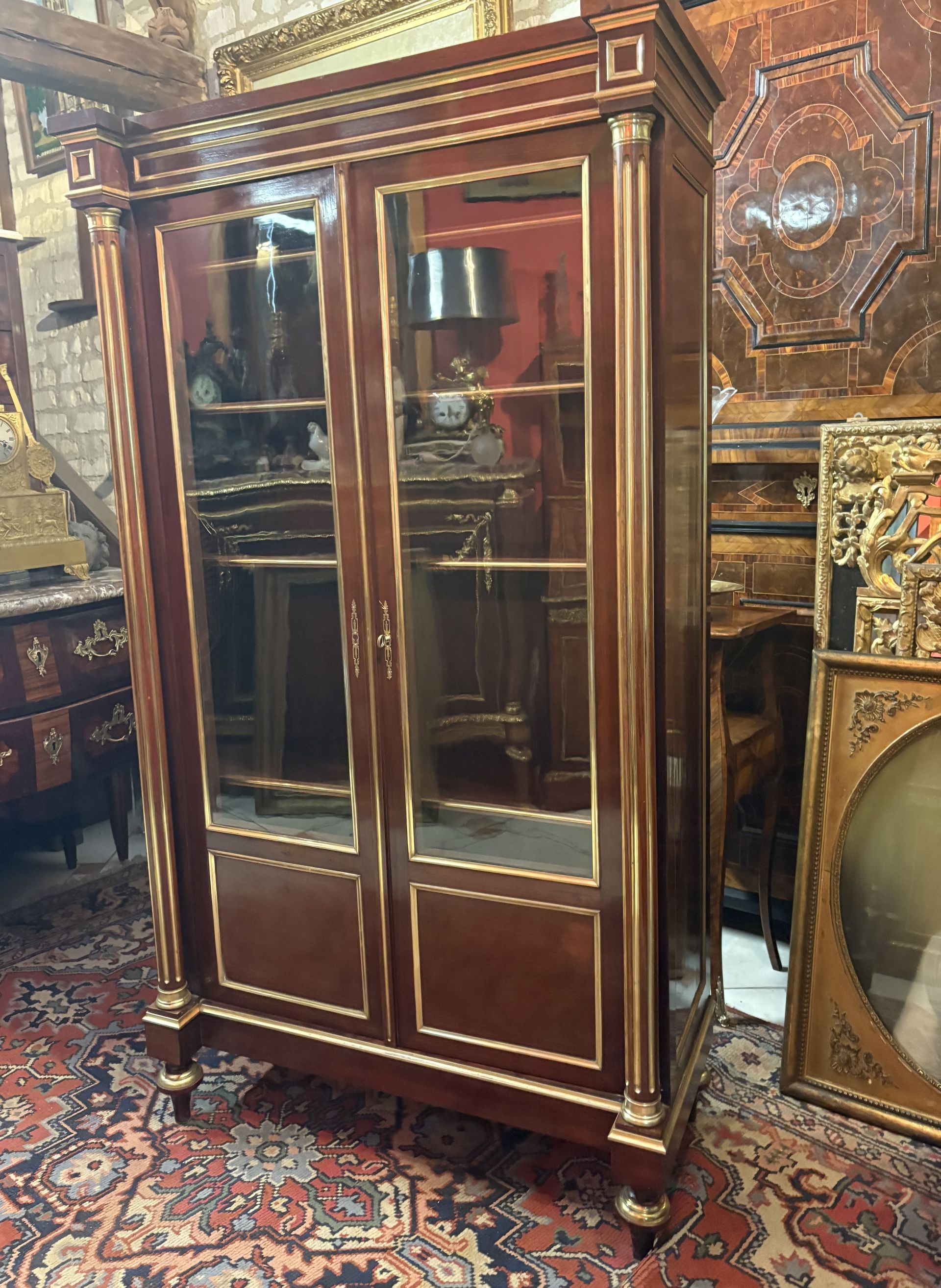 BIBLIOTHEQUE - VITRINE DE STYLE LOUIS XVI - 19ème EN ACAJOU ET FILET DE LAITON Elle présente une riche ornementation de laiton doré dans les encadrements des portes, les vitres , sur les côtés,  sur la corniche et les pieds. Montants à cannelures Incrustés de laiton doré. Elle ouvre par deux portes vitrées aux deux tiers laissant apparaitre un intérieur possédant quatre étagères réglables. Le tout reposant sur quatre pieds toupies. Possède sa clé. Cette bibliothèque est en parfait état.