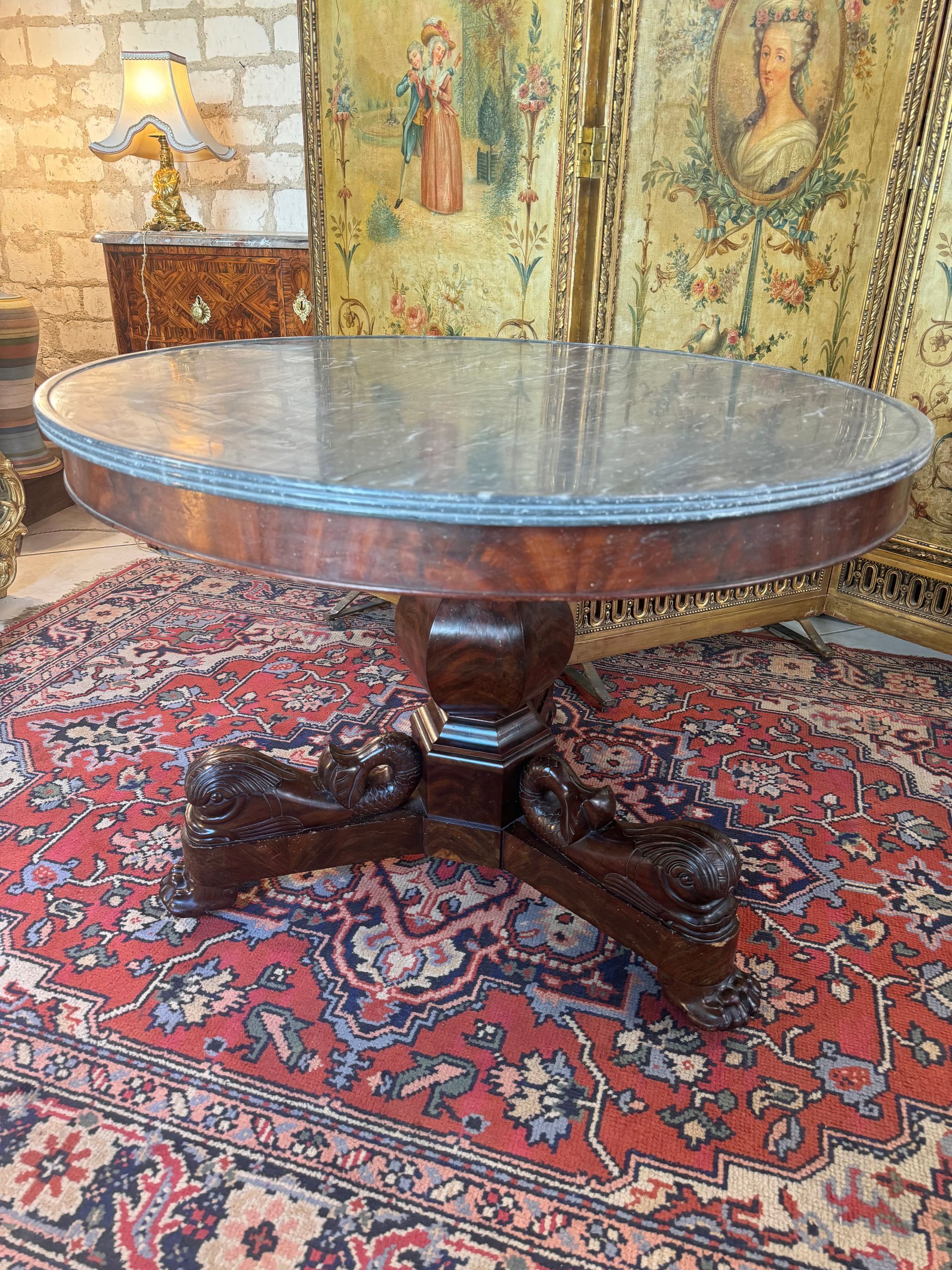 Guéridon Empire en placage d’acajou et acajou massif.
Il repose sur un piétement tripode qui se termine par des pieds représentant des dauphins sculptés.
le tout coiffé  d’un beau marbre bleu turquin.
Ce guéridon possède des roulettes.