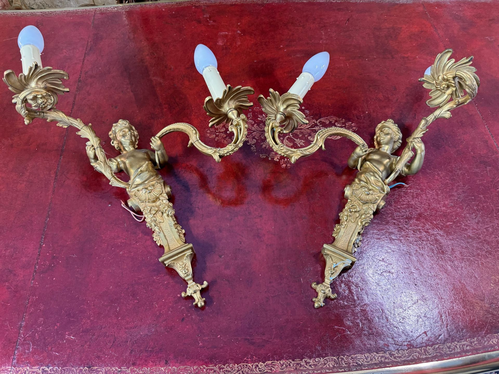 Paire d'appliques murales de style Louis XV - fin 19ème, à deux bras de lumières, en bronze doré finement ciiselé.
Cette paire d'appliques représente chacune un buste d'enfant vêtu d'un drapé agrémenté d'un décor floral soit des petites fleurs, tenant en main les bras de lumière.
Appliques électrifiées.