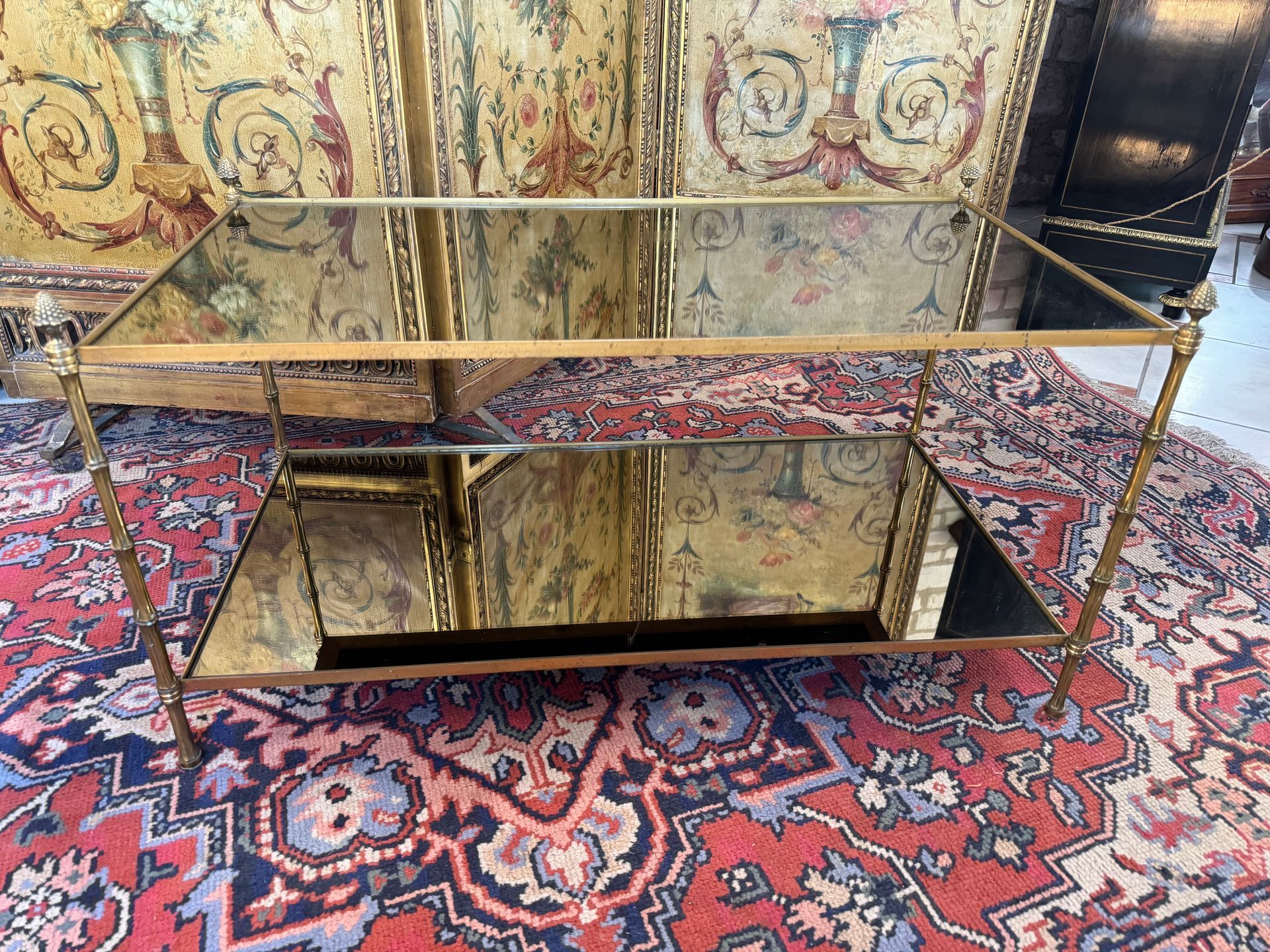 Table basse à double plateau en verre églomisé et laiton doré, 
le piètement à décor de forme bambou se terminant par des pommes de pin.