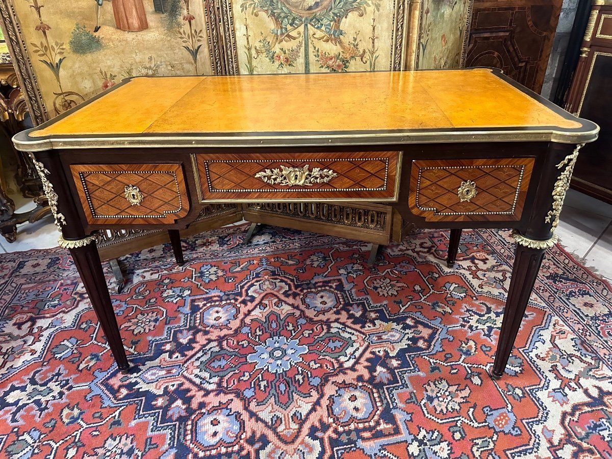 Elégant bureau plat rectangulaire de style louis XVI,
En marqueterie à la reine, fleurs dans les croisillons,
Ce bureau est toute face, ouvre par trois tiroirs en façade et repose sur des pieds fuselés cannelés,
Il présente un décor de bronze sur les montants représentant un noeud  floral ainsi que sur la serrure du milieu, frise de perles sur le pourtour des tiroirs.
Dessus recouvert d’un cuir havane en bon état.
Meuble attribué à l’ébéniste français : François Linke.