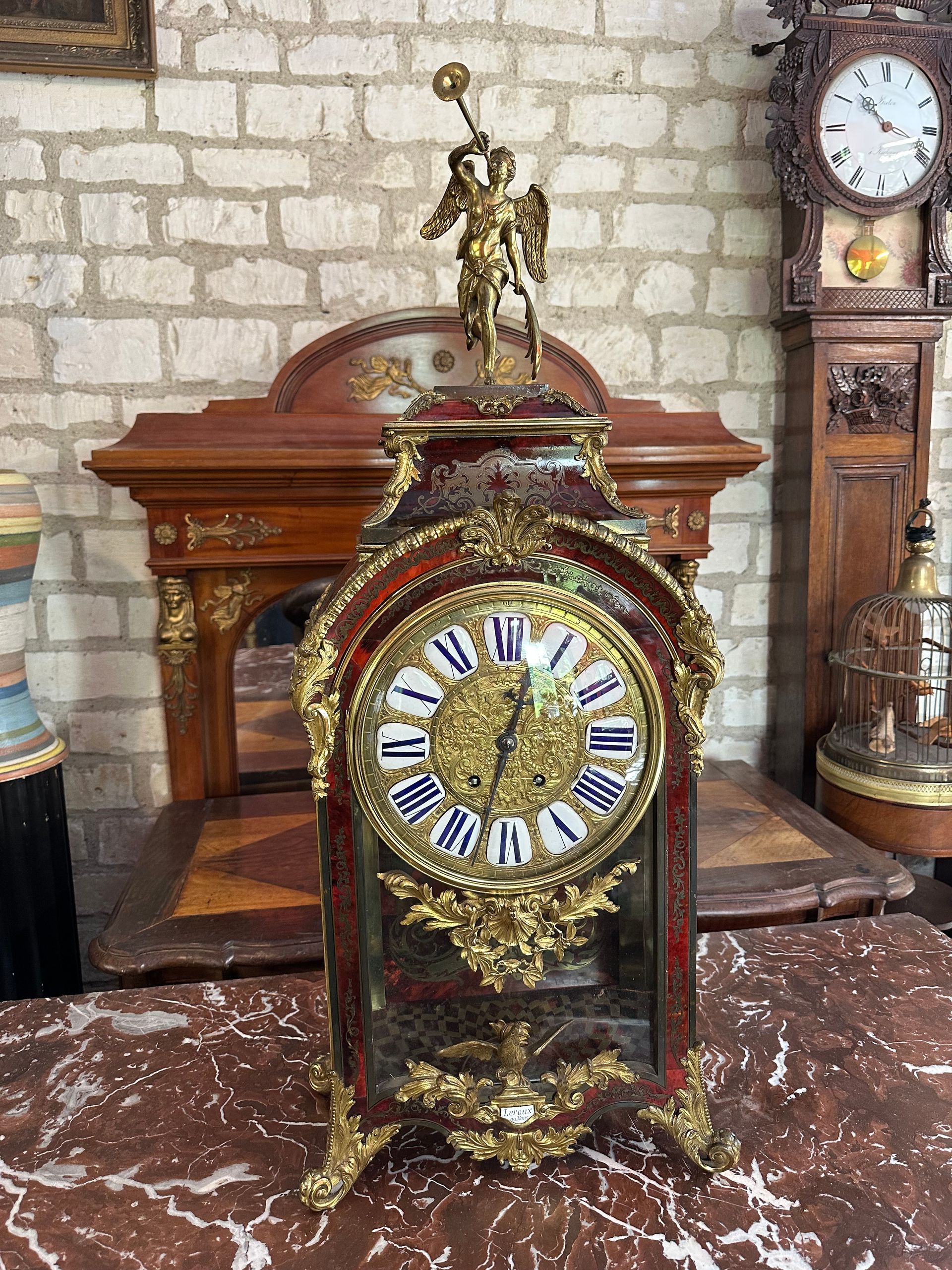 CARtTEL BOULLE Il est de forme rectangulaire en marqueterie de boulle de laiton gravé et écaille teintée rouge, les angles sont soulignés de chutes feuillagées , pieds à feuilles d’acanthe et enroulement, Cadran à chiffres romains, orné de douze cartouches émaillées blanc,  surmonté d’un coq déployant ses ailes, perché sur une cartouche signé LEROUX/AU  MANS, figure renommée, Platine portant le cachet VINCENTI ET CIE Médaille d’argent 1855. Balancier soleil.