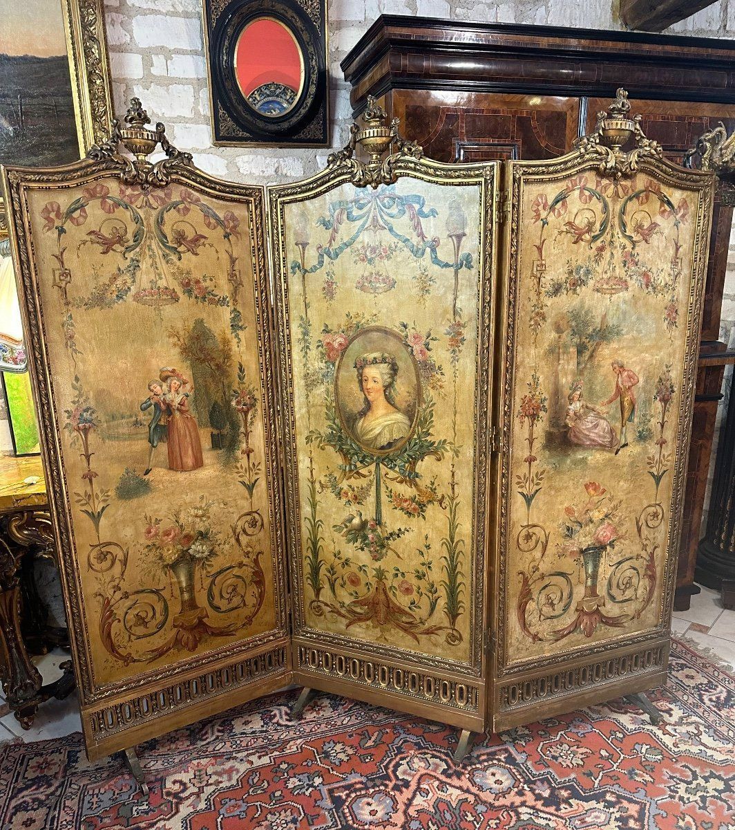 Grand et superbe paravent d’époque XIXème ,de style Louis XVI, avec miroirs.
Ce paravent de scènes romantiques à décor Louis XVI est composé de trois grandes huiles sur toile réunies par une boiserie en bois doré , sculptée 
- chaque vantail extérieur représente une scène galante dans le gout de la cour de Versailles, avec différents décors :  vase de fleurs, composition florale, feuillages et arabesques,
- Le vantail du milieu représente le portrait de Marie-Antoinette encadré de forme médaillon avec un décor floral, de colombes, flambeaux et nœud Louis XVI.
Chaque vantail est surmonté d’une urne surplombée d’une flamme,  pourtour de frise, motif de fleurs et autre et base à décor ajouré.
La rareté de ce paravent est qu’il présente en arrière de grands miroirs d’origine sur chaque vantail.
Le tout supporté par des pieds avec roulettes.
Exécution soignée et de bonne facture, les couleurs sont harmonieuses et fraiches, belle hauteur.
L ‘ensemble et la structure sont en bon état d’origine. .