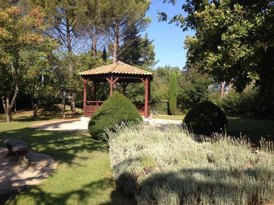 Une gloriette en bois dans un jardin ensoleillé, avec des buissons soigneusement taillés et des plants de lavande.