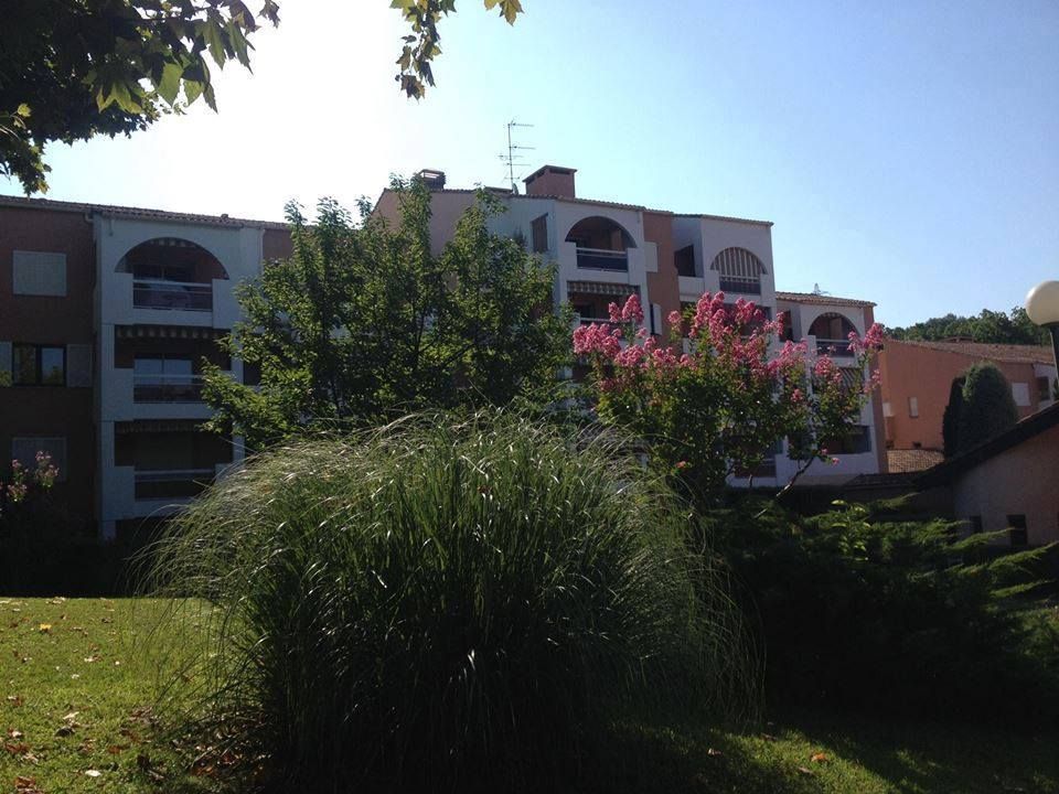 Immeuble d'appartements avec balcons et toits voûtés, vu depuis une pelouse arborée et parsemée d'arbustes.