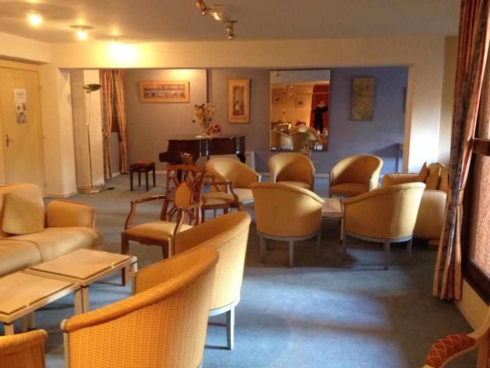 Salle d'attente confortable avec chaises jaunes, canapé, petites tables, piano et œuvres d'art.