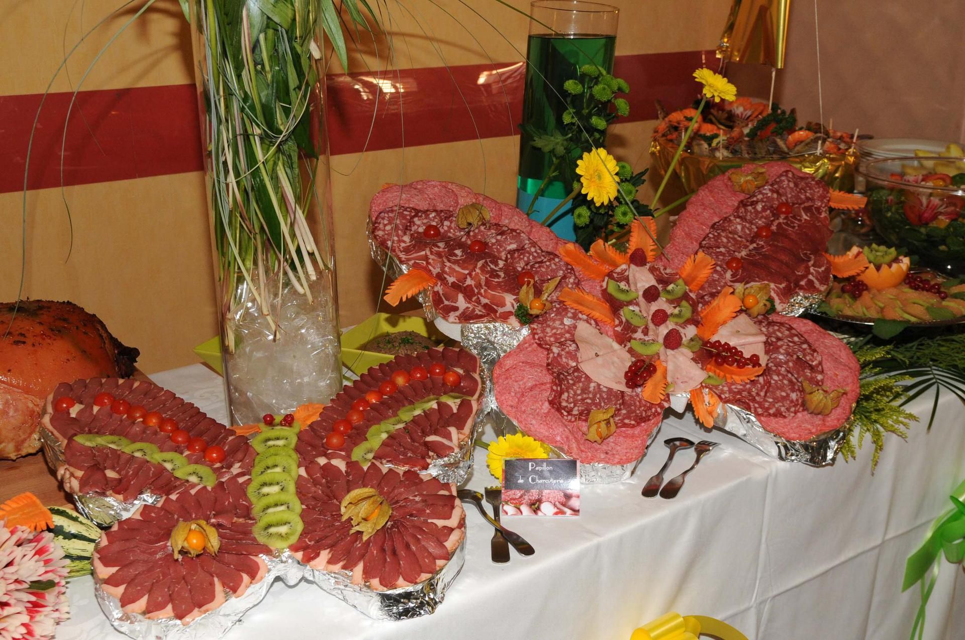 Planches de charcuterie en forme de papillon sur un buffet, décorées de fruits et de fleurs.