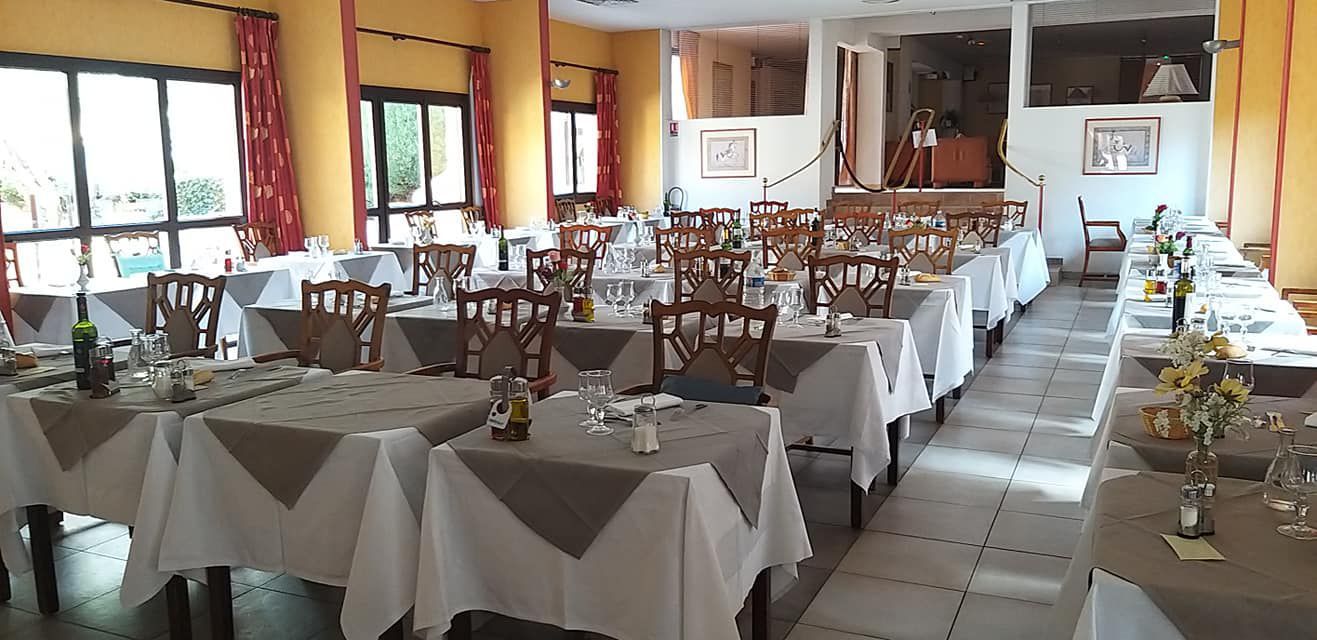 Salle à manger du restaurant avec tables dressées pour le service ; nappes blanches, accents aux tons neutres et chaises.
