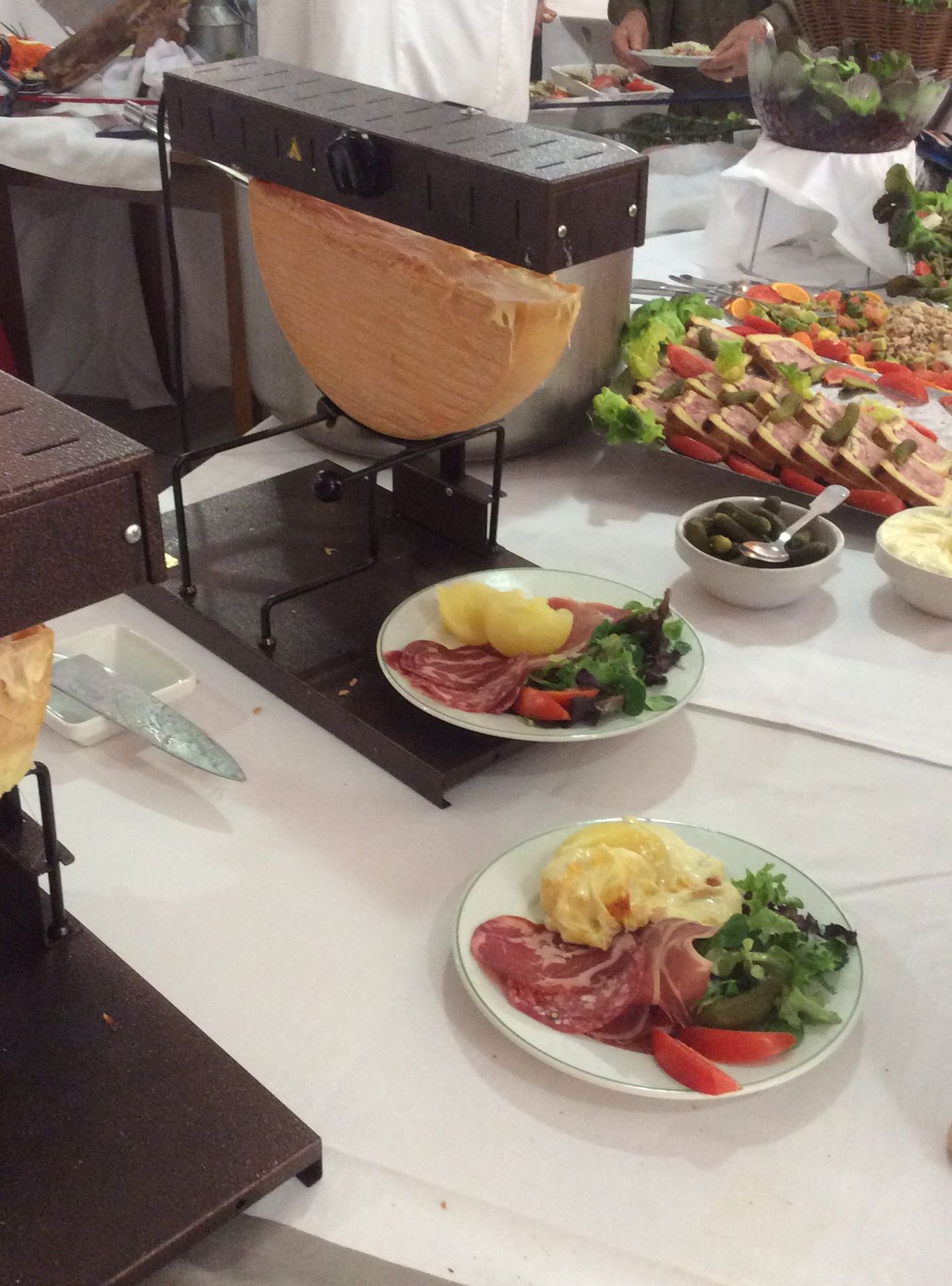 Fromage à raclette en train de fondre, servi avec des pommes de terre, de la viande et de la salade dans des assiettes. 