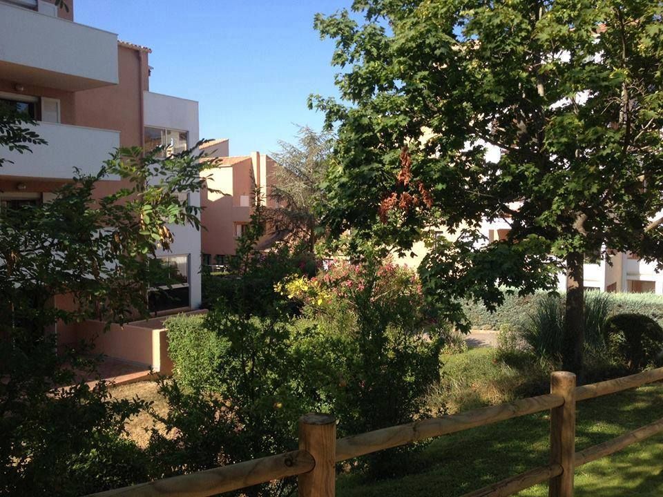 Des immeubles d'appartements derrière une clôture en bois, avec des arbres et des buissons.