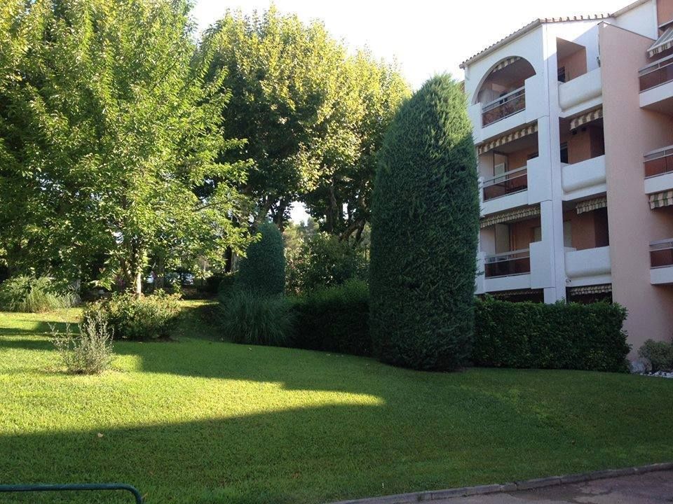 Pelouse verdoyante luxuriante avec arbustes et arbres taillés, jouxtant un immeuble d'appartements à plusieurs étages.