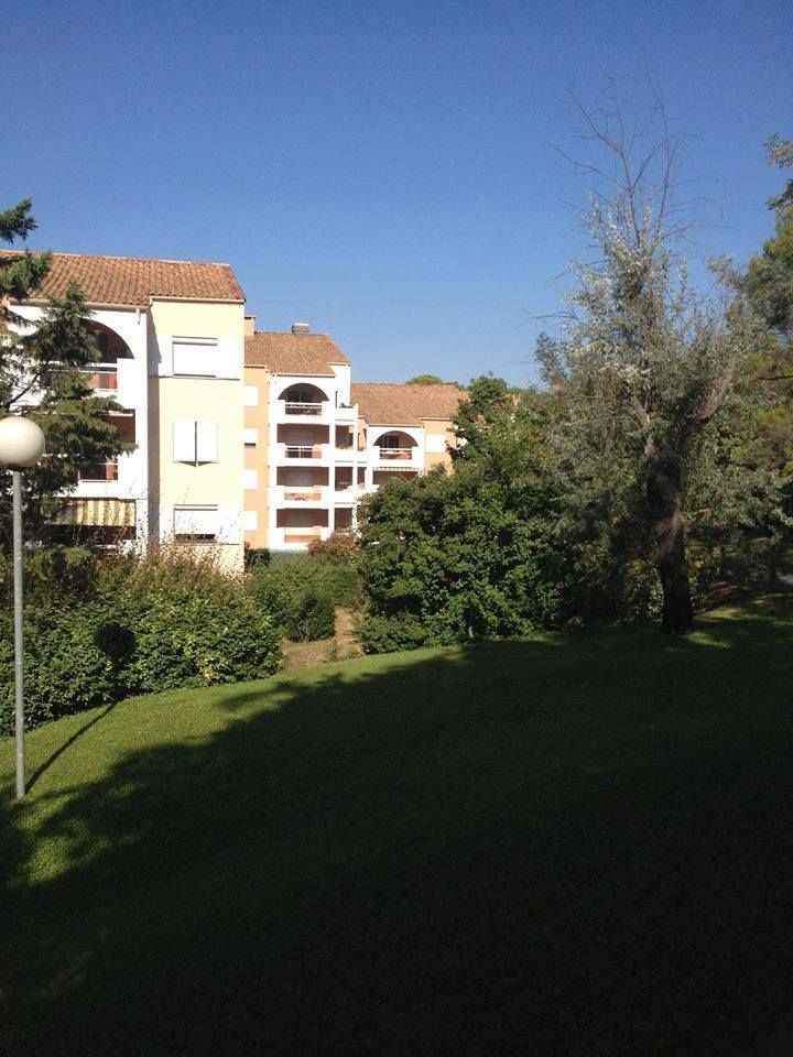 Immeubles d'appartements avec balcons, murs clairs, toits de tuiles rouges, derrière des pelouses verdoyantes et des arbres.