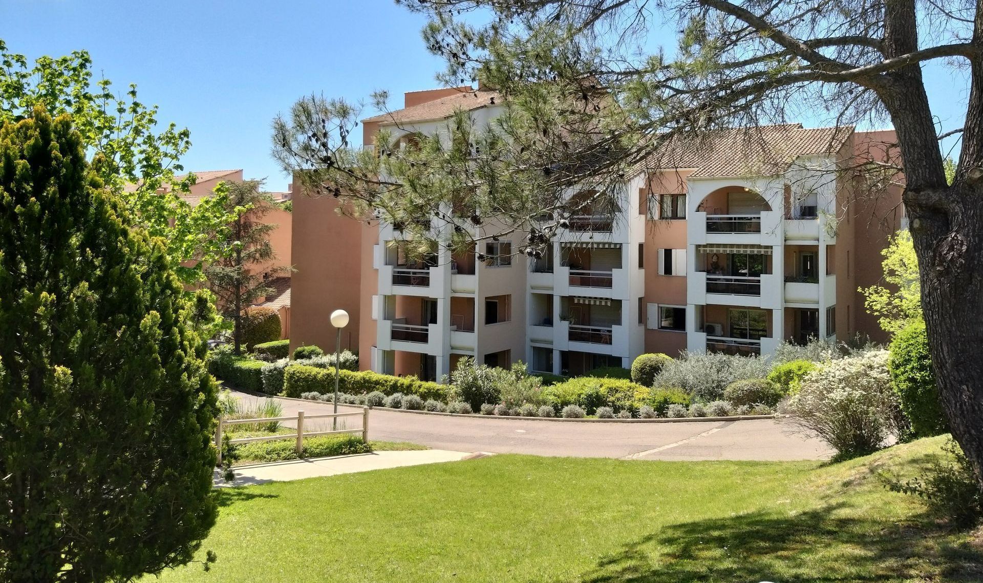 Immeuble d'appartements avec balcons, vu depuis une pelouse verdoyante arborée.
