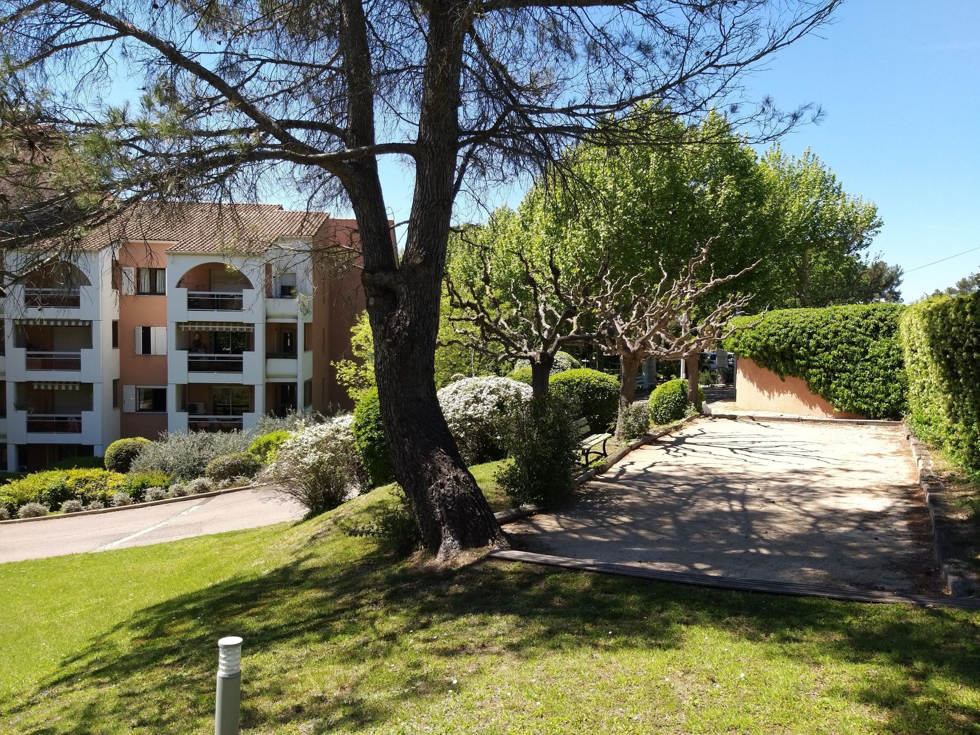 Vue extérieure d'un immeuble d'appartements avec balcons, arbres, pelouse et allée de gravier.
