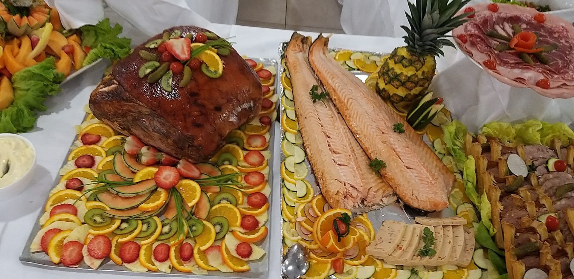 Un buffet présentant un jambon glacé et du saumon, garnis de fruits et de légumes.