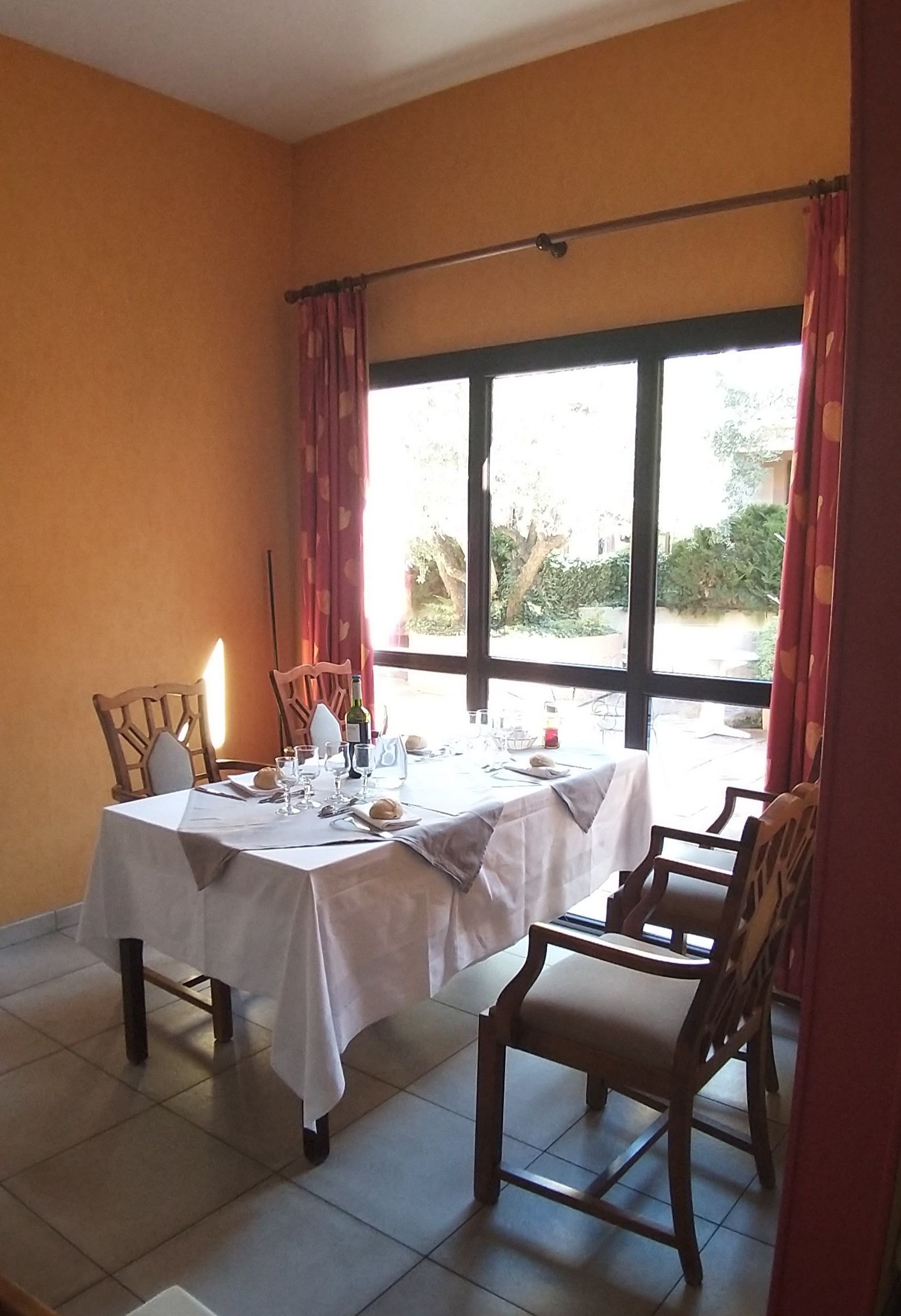 Table à manger dressée pour un repas près d'une fenêtre aux rideaux rouges. 
